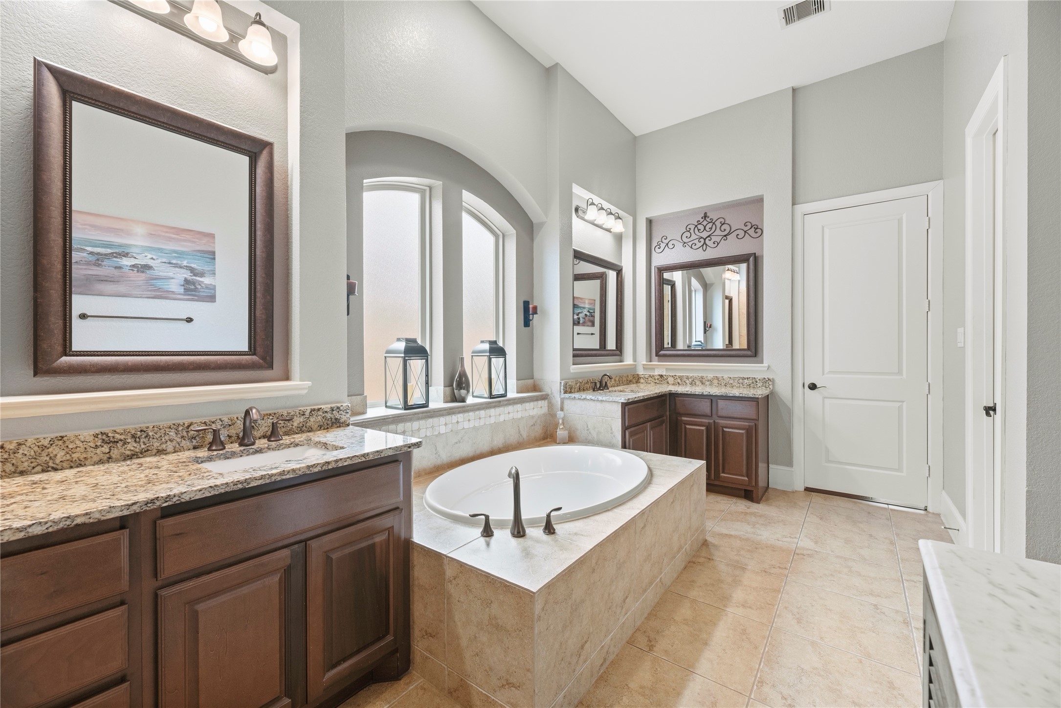 Beautiful primary bathroom featuring a large soaking tub, split vanities, granite countertops, and beautiful cabinetry.