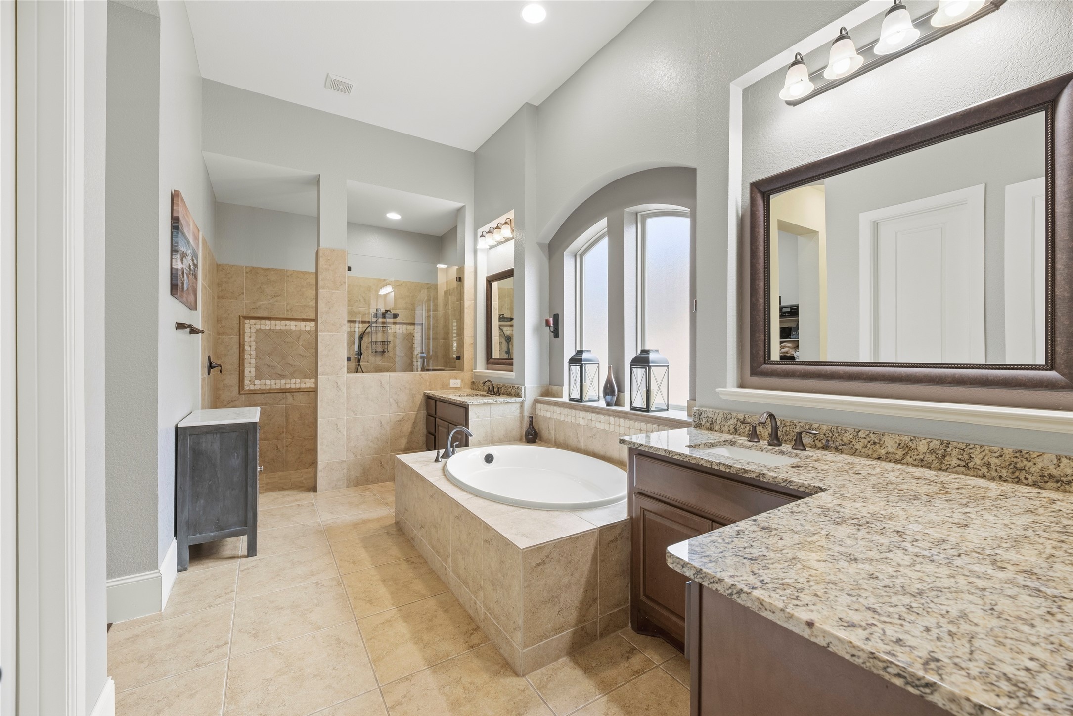 Beautiful primary bathroom featuring a large soaking tub, split vanities, granite countertops, and beautiful cabinetry.
