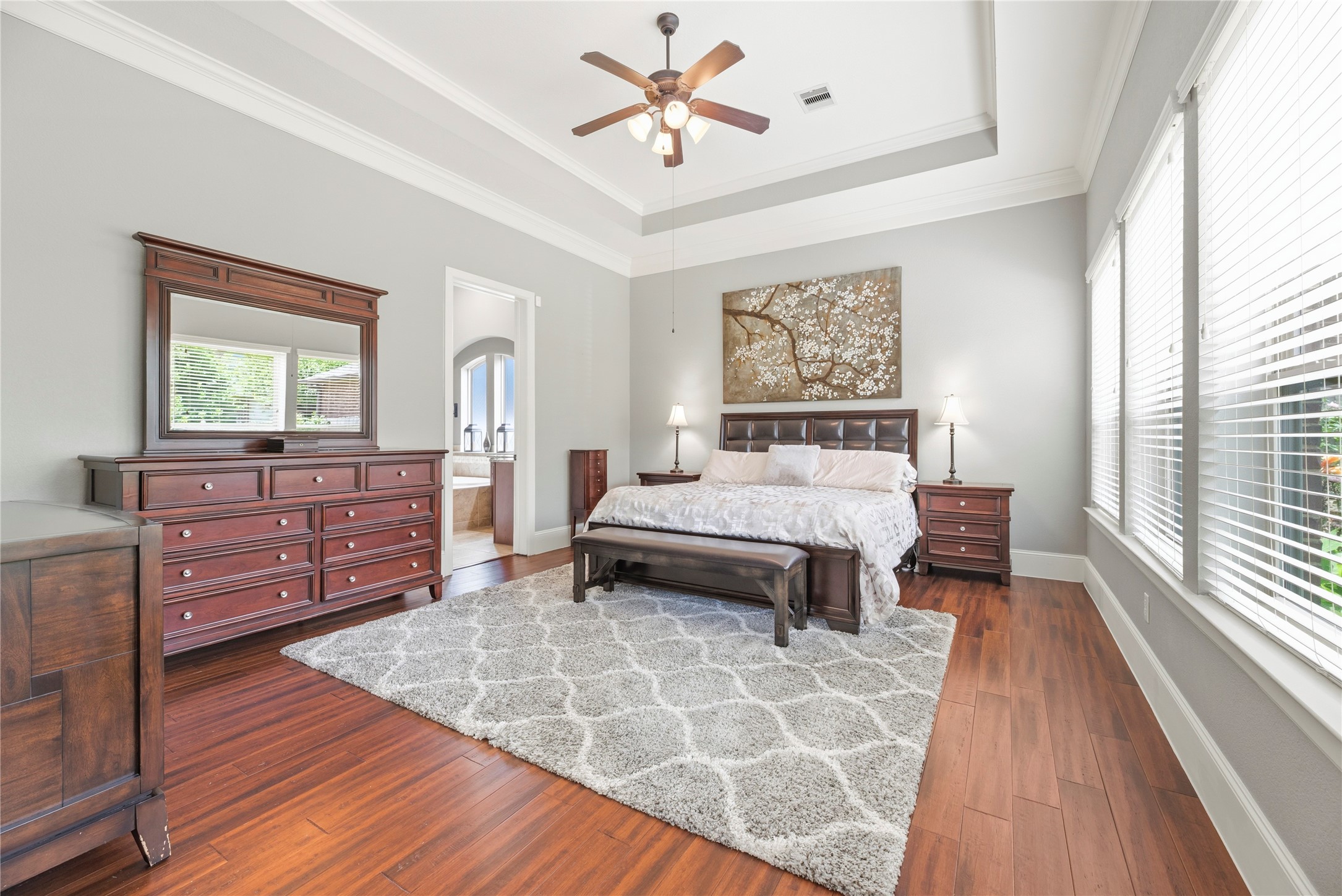 Spacious primary suite with wood floors, coffered ceilings, sleek paint, and large windows overlooking your private backyard oasis.