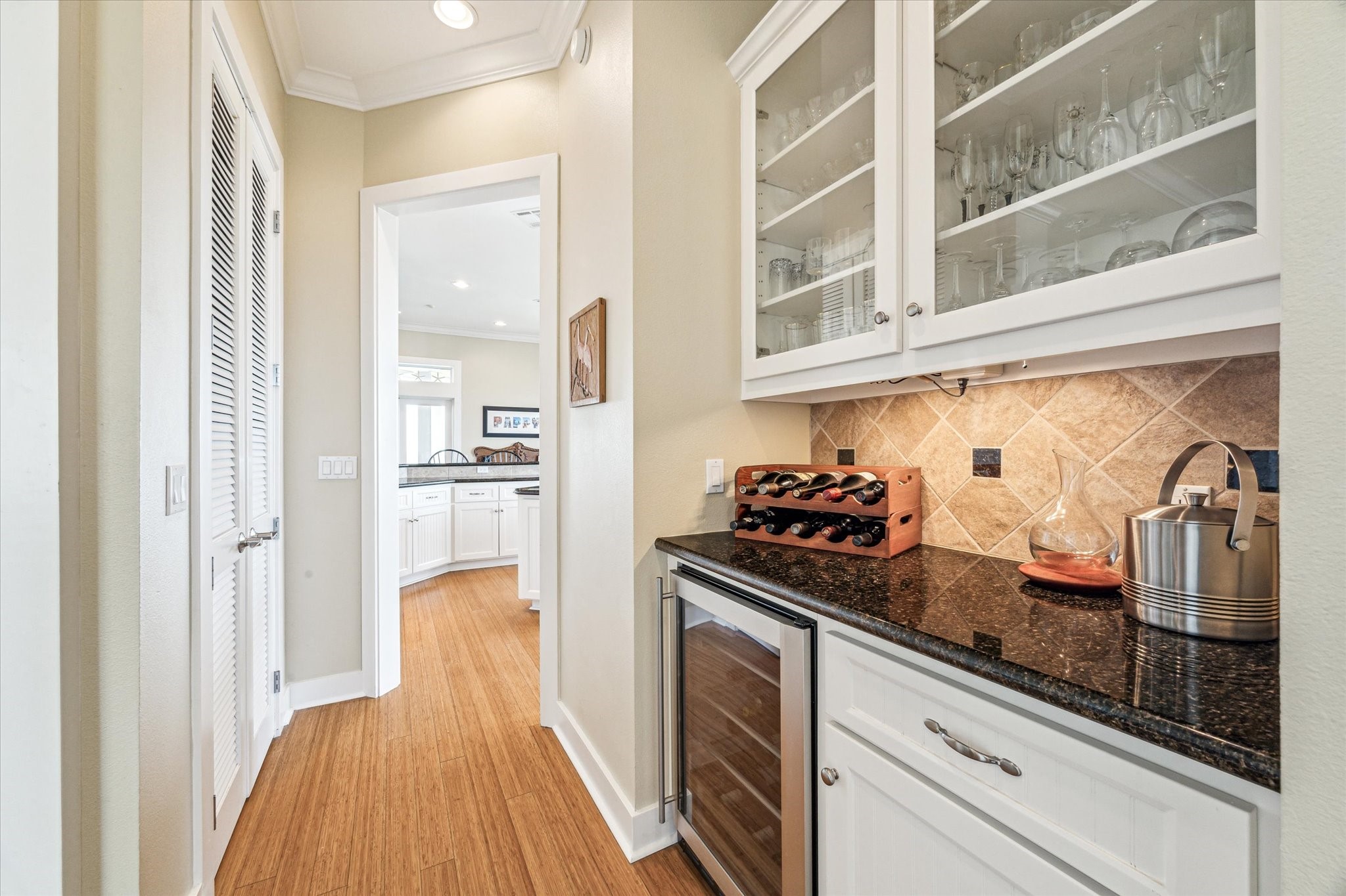 Large butlers pantry enhances the kitchens functionality, featuring a wine cooler for effortless entertaining, elegant glass-front cabinetry for display, and under-cabinet lighting that adds both ambiance and practicality