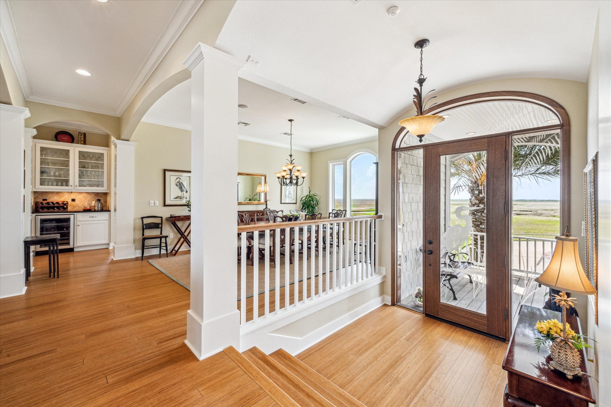 This elegant entryway is filled with abundant natural light streaming through a large arched glass door. Classic architectural details, including column accents and wide trim, lend a sense of timeless elegance throughout this coastal retreat