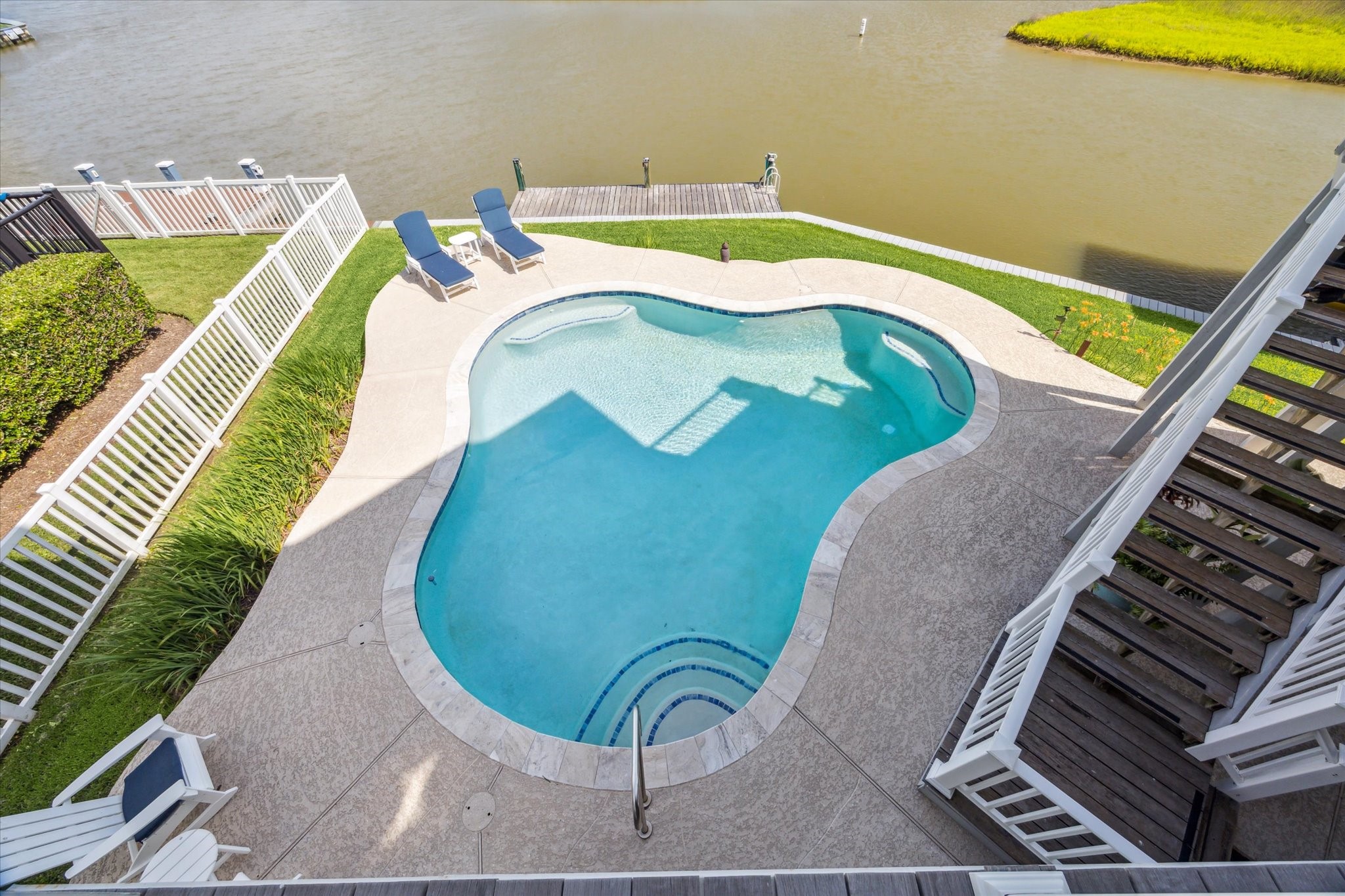 This aerial view showcases a beautifully designed, swimming pool set along a waterfront backdrop. The pool is surrounded by a spacious deck with ample room for lounging