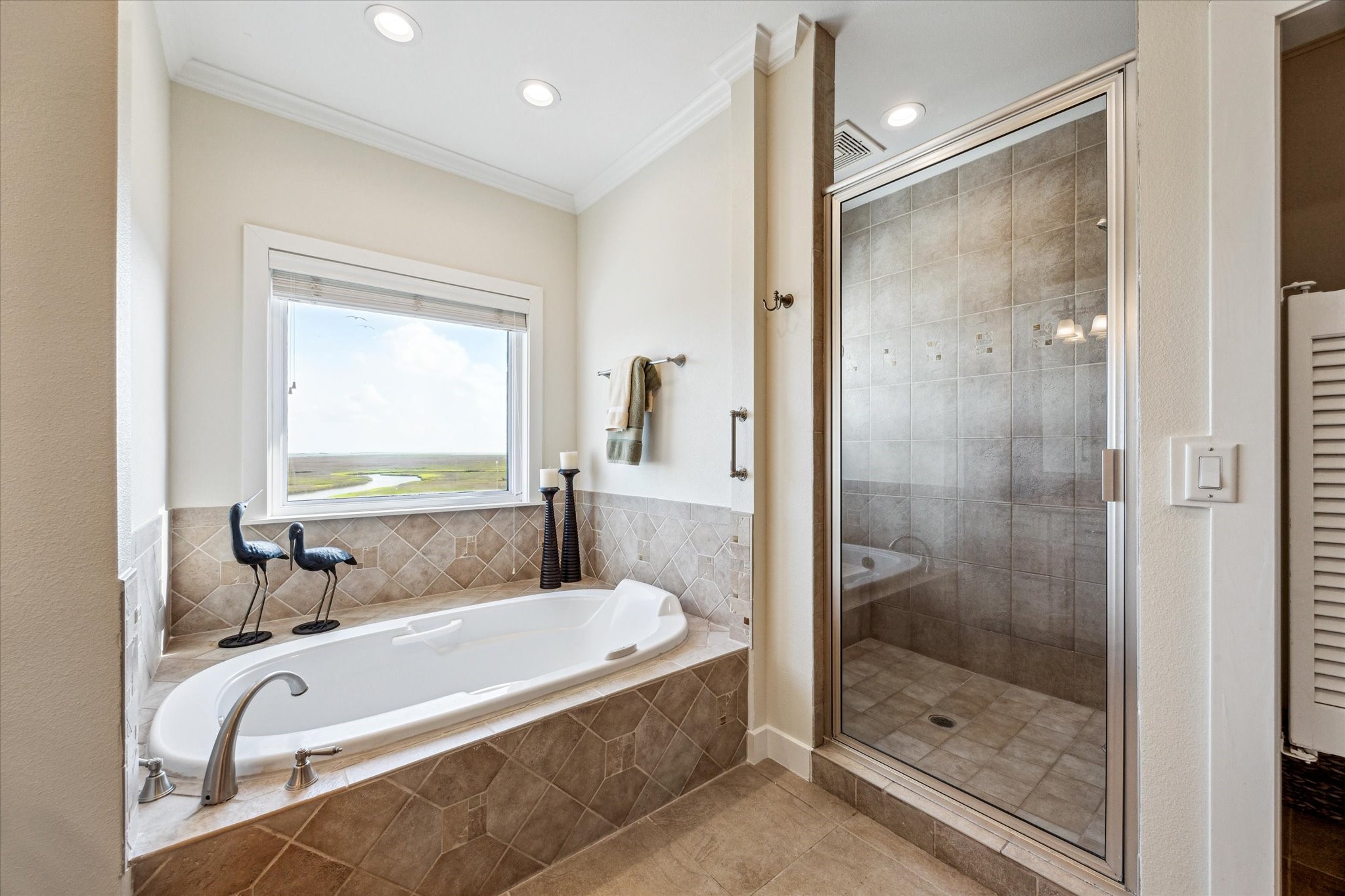 The primary bathroom features a luxurious Bain garden tub with an air bubbler for a spa-like experience, while the spacious shower offers stunning views of the surrounding waters and coastal wetlands. A separate glass-enclosed shower adds function and style, creating a relaxing and beautifully finished retreat