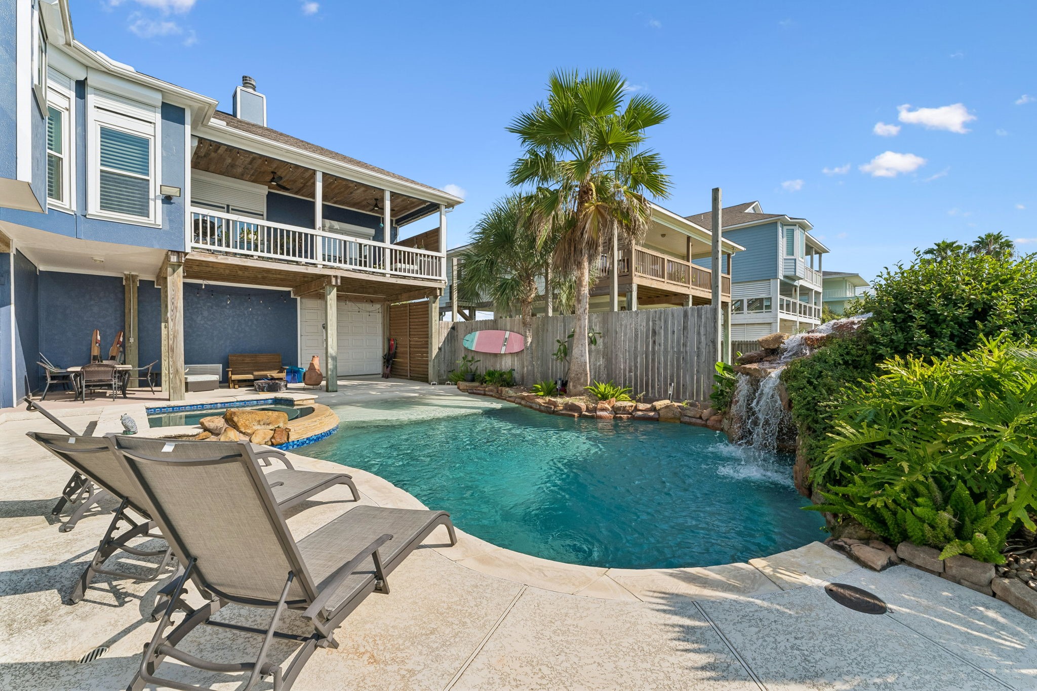 Private backyard oasis pairs a sparkling pool with lush tropical landscaping and a cascading rock waterfall. Expansive decking offers plenty of room to lounge, entertain, and enjoy the coastal sunshine.