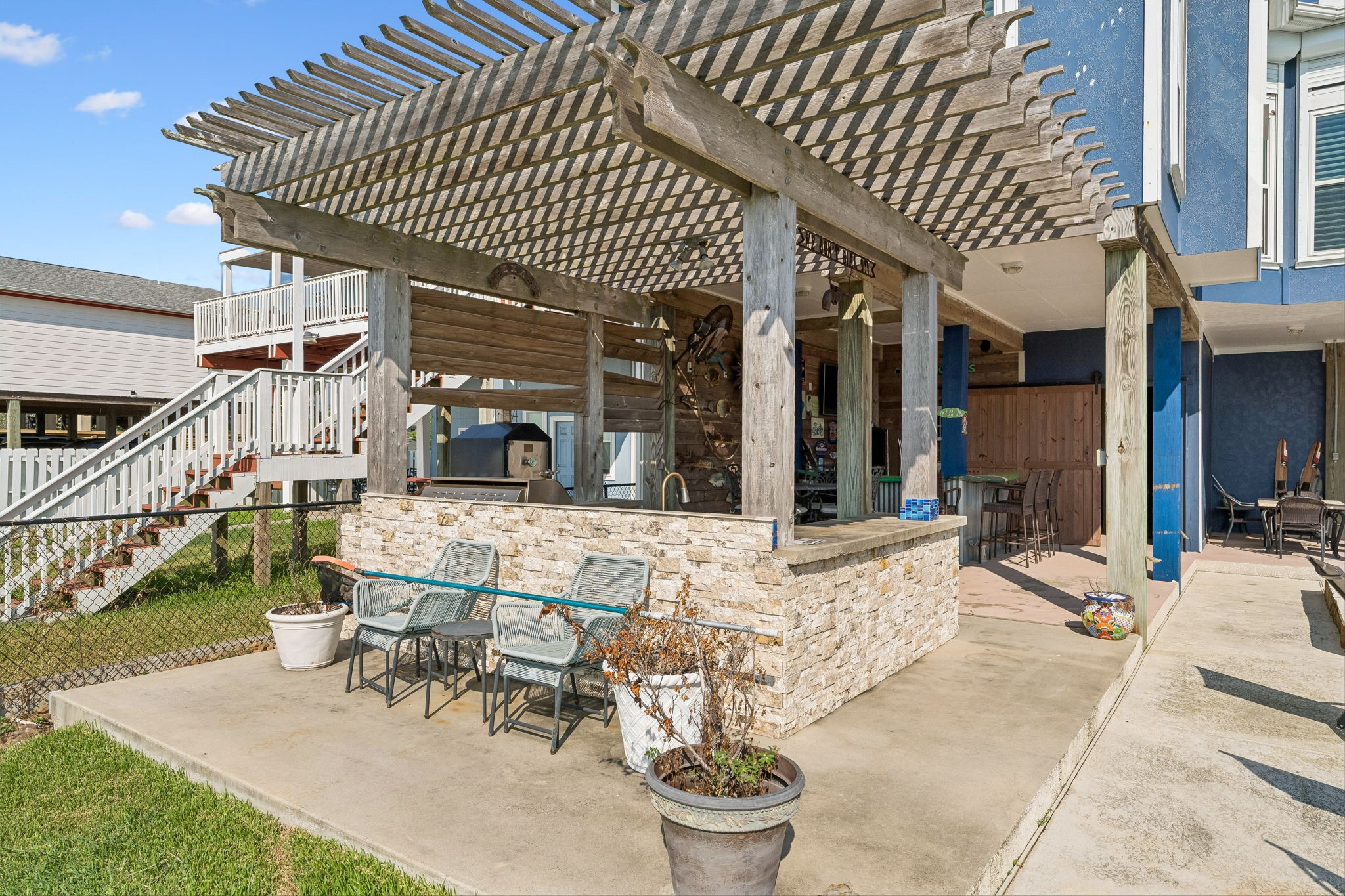 Pergola covered patio extends the outdoor entertaining space with additional seating beside the kitchen and bar. Stone accents and open air design create an inviting place to gather near the waterfront.