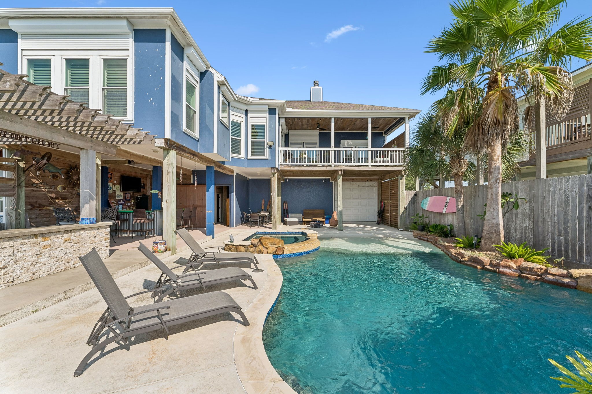 Expansive poolside setting showcases the homes covered outdoor living areas and upper balcony overlooking the backyard. Multiple gathering spaces create an effortless setup for enjoying the Galveston Bay lifestyle.