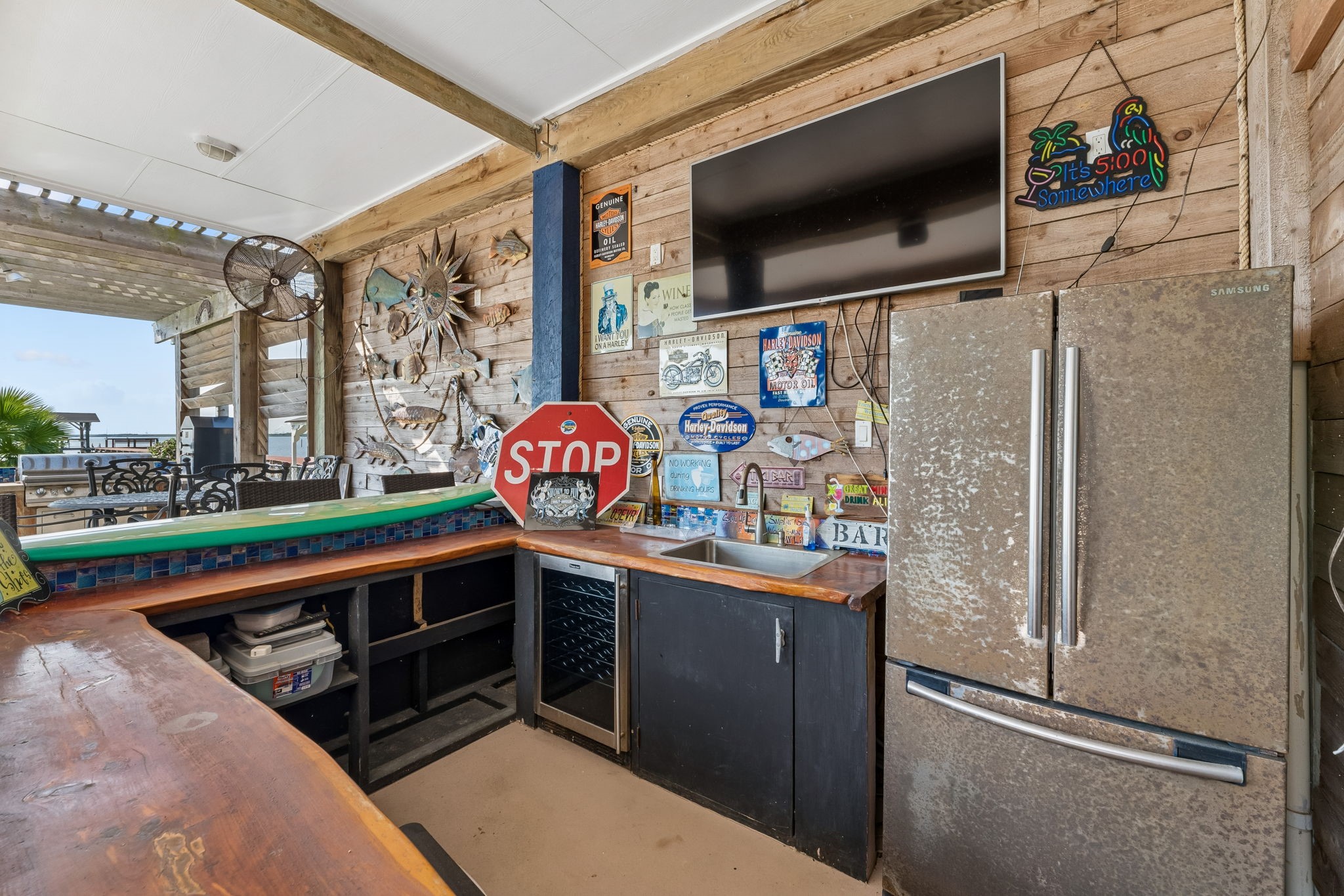 Fully equipped outdoor bar features a sink, full size refrigerator, mounted TV, and generous counter space. Rustic wood finishes add character to this inviting entertainment zone.