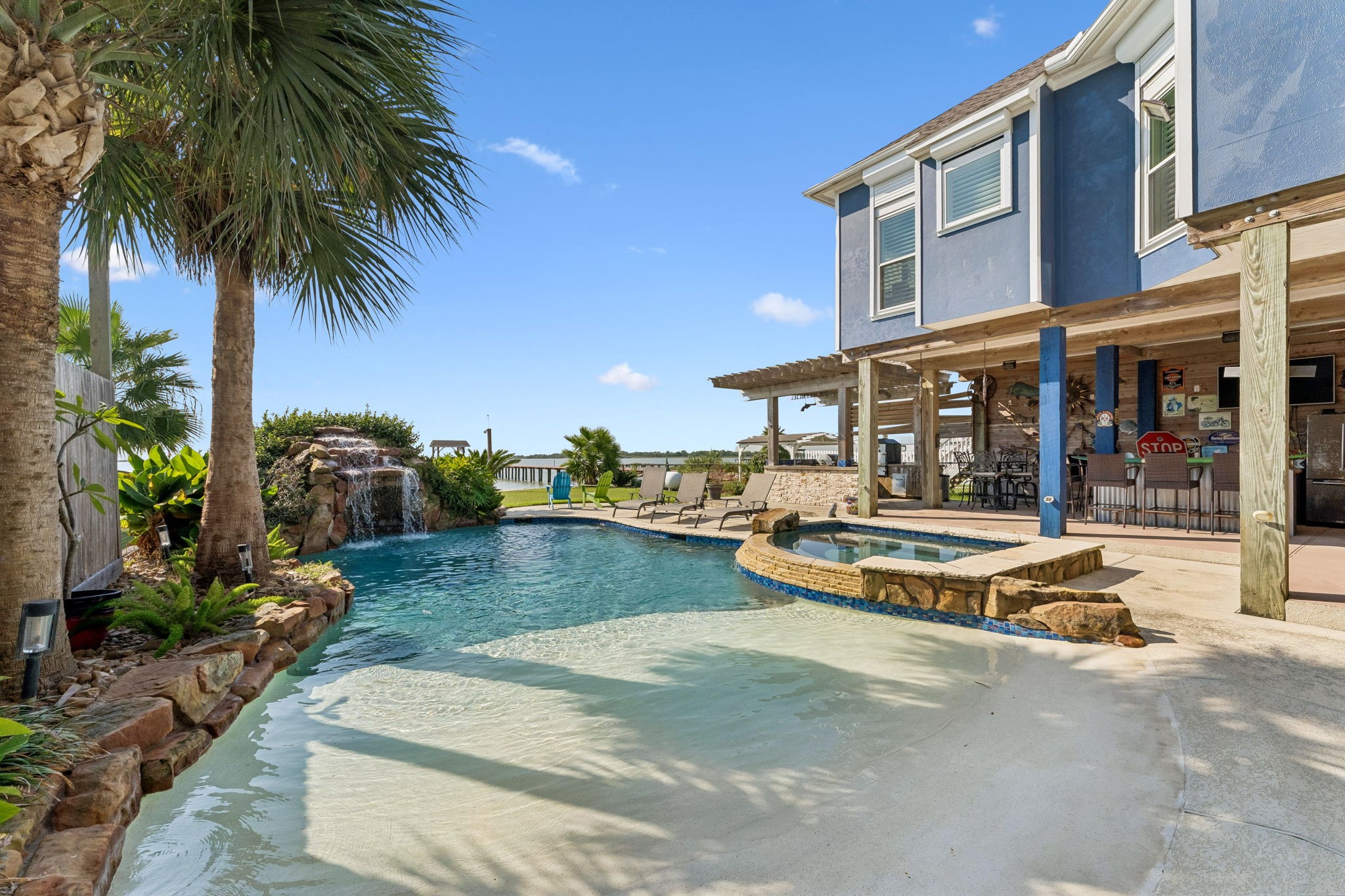 Resort-style pool with a built-in hot tub, waterfall feature, and lush tropical landscaping. The covered outdoor kitchen and bar create the perfect setting for poolside entertaining Resort-style pool with a built-in hot tub, waterfall feature, and lush tropical landscaping. The covered outdoor kitchen and bar create the perfect setting for poolside entertaining