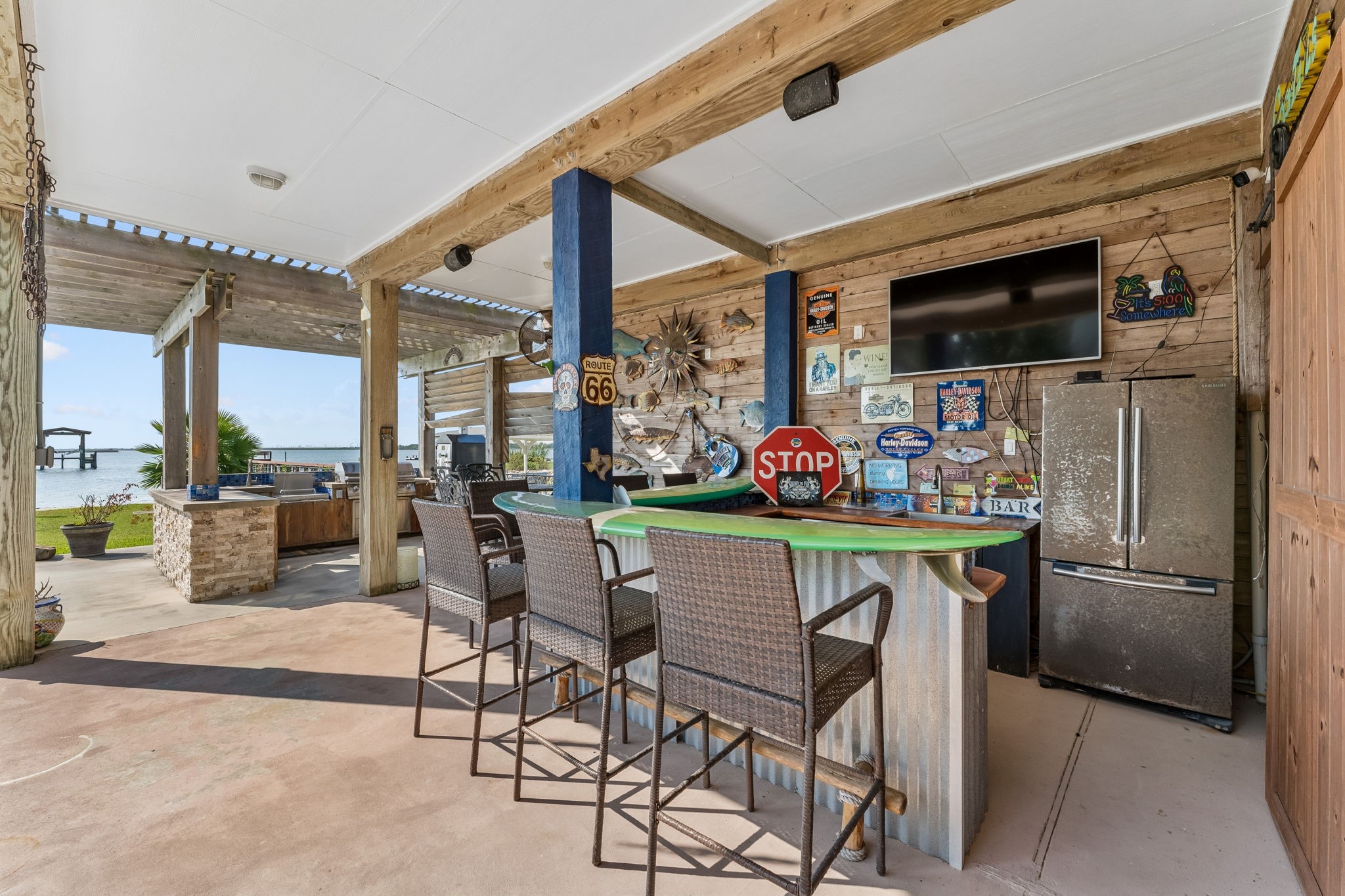 Covered outdoor bar creates a fun gathering spot with generous seating, a refrigerator, and mounted TV. Just steps from the bay, it is perfectly positioned for effortless waterfront entertaining.