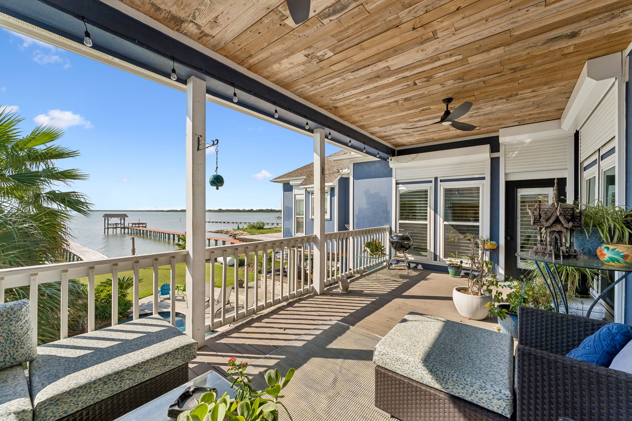 Expansive covered balcony frames sweeping views of Galveston Bay and the private pier below. A wood plank ceiling and generous seating area create an ideal setting for waterfront relaxation.