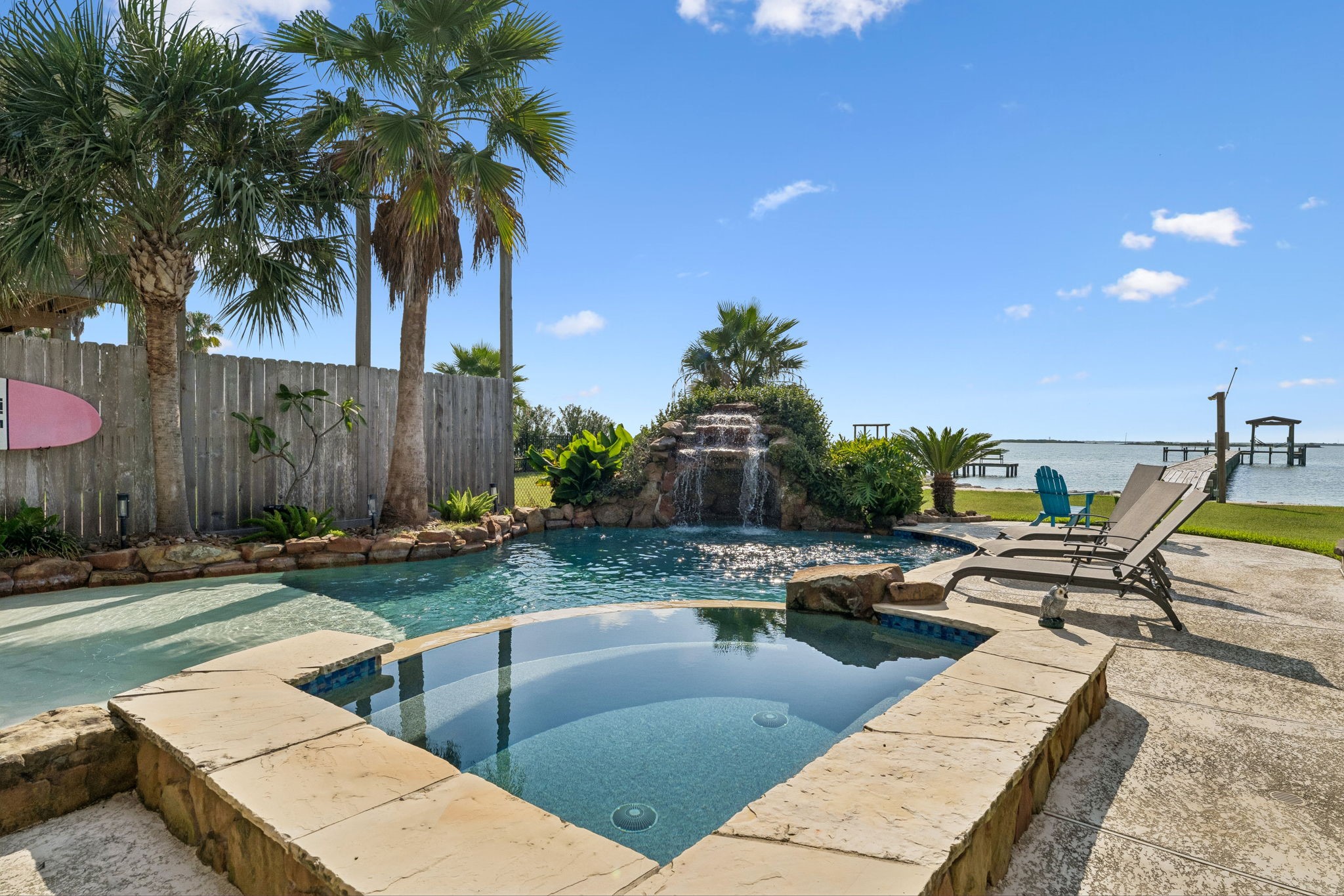 Sparkling pool and hot tub overlook the bay, creating a picture perfect backdrop for coastal living. A cascading rock waterfall and tropical palms complete the backyard oasis. Sparkling pool and hot tub overlook the bay, creating a picture perfect backdrop for coastal living. A cascading rock waterfall and tropical palms complete the backyard oasis.
