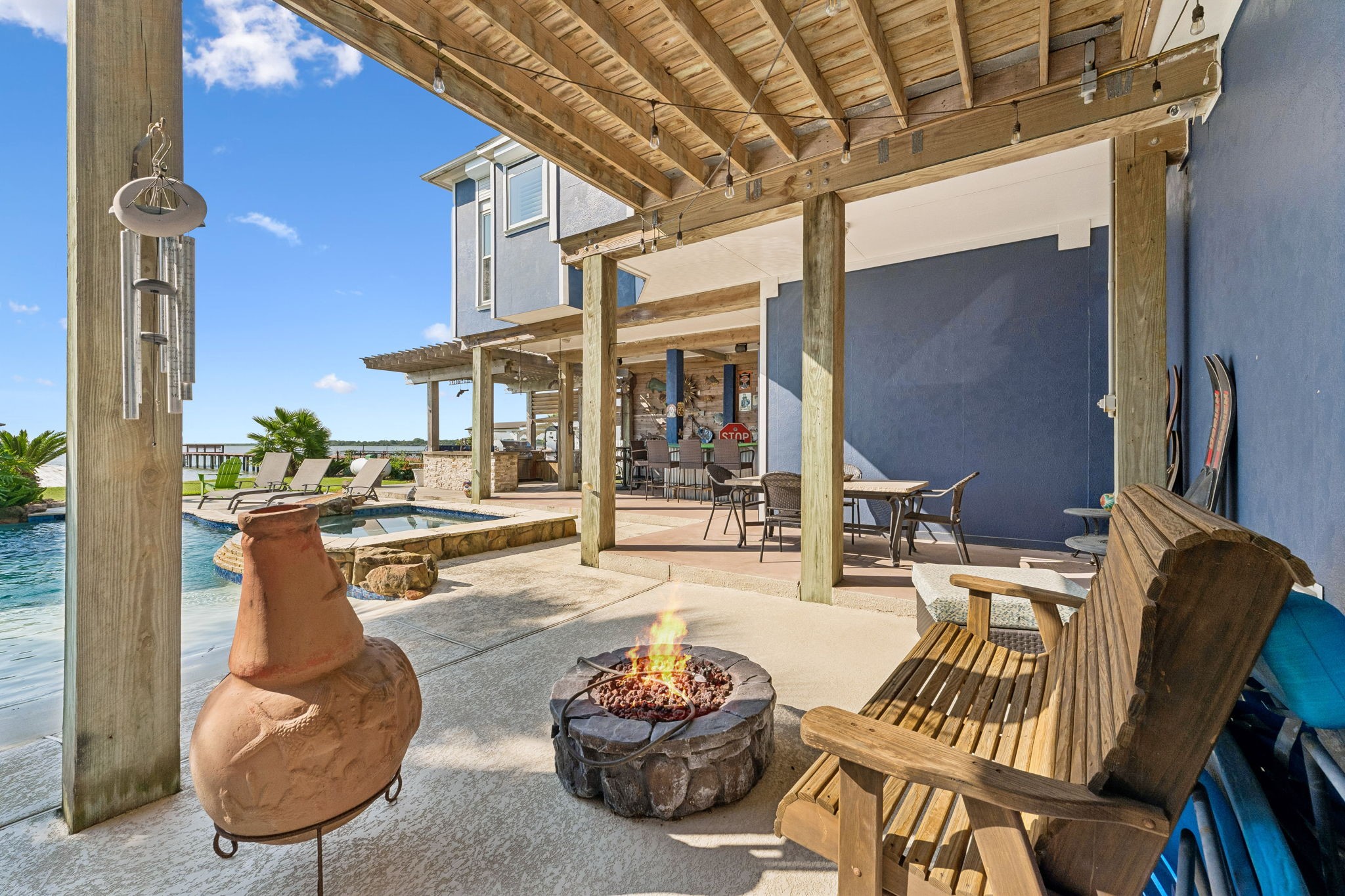 Cozy fire pit area creates the perfect spot to unwind beside the pool and waterfront. Covered seating nearby extends the outdoor living experience from day into evening.