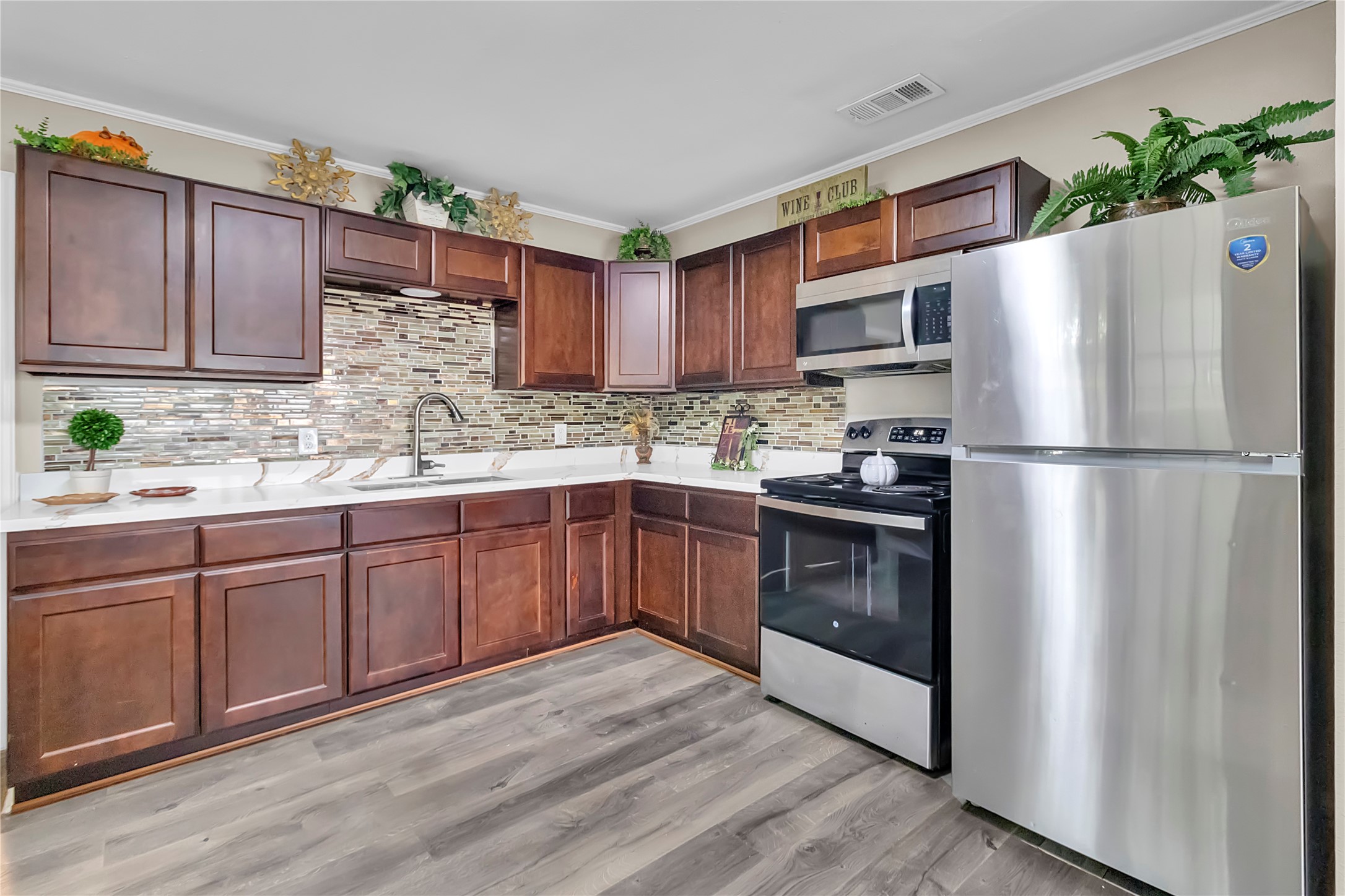 Attractive kitchen featuring abundant cabinet storage, stainless-steel appliances, updated flooring, and decorative tile backsplash.