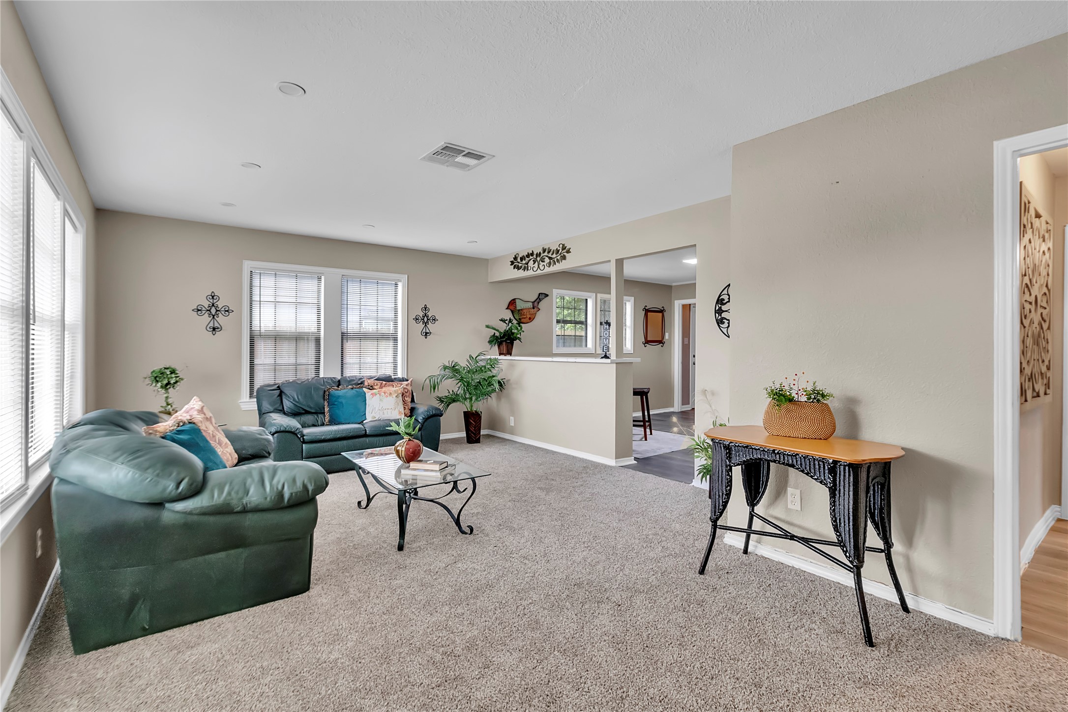 Spacious living room with fresh carpet, large windows, and an open connection to the kitchen and adjoining living spaces.