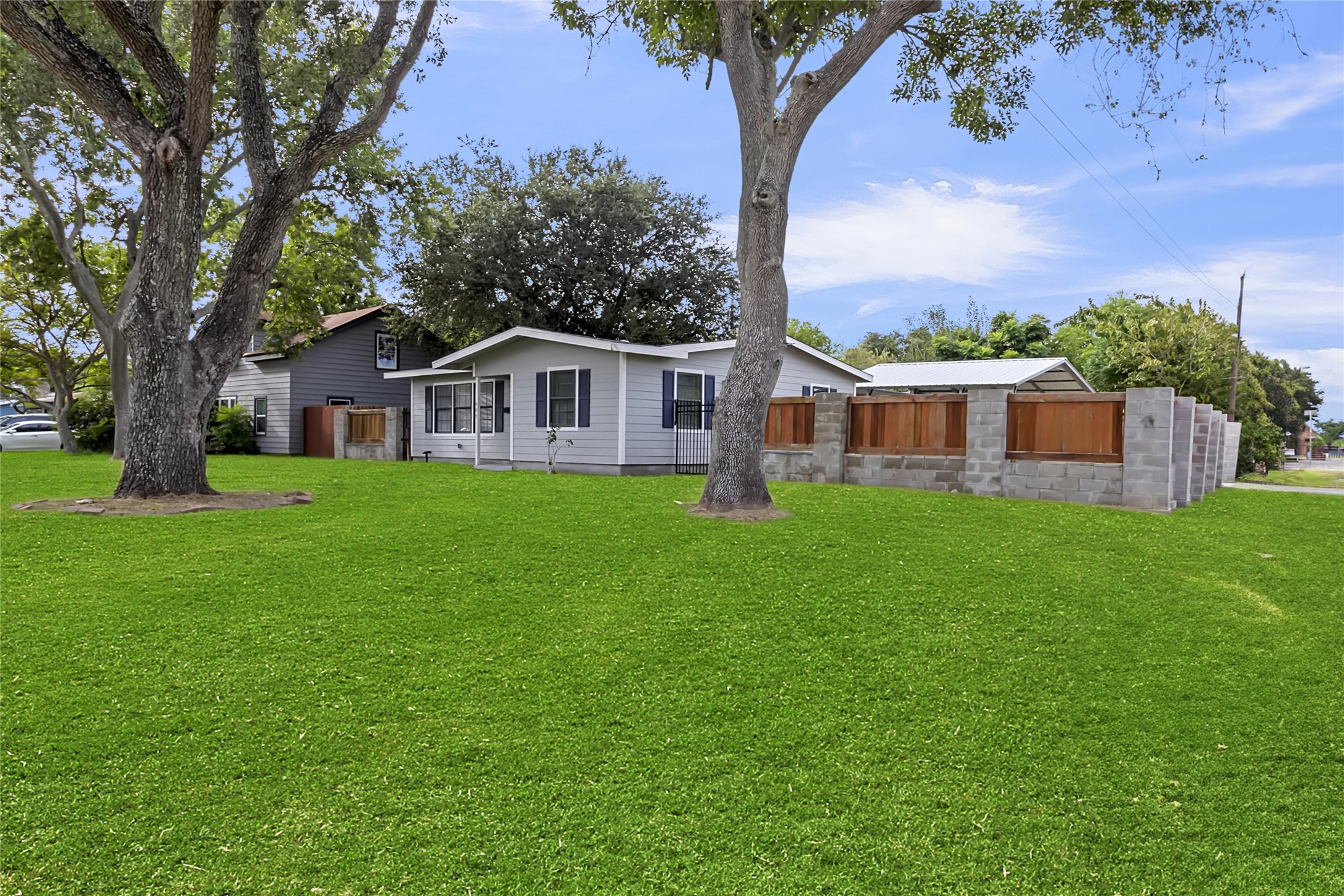 Wide exterior view showcases the large corner lot, mature shade trees, expansive lawn, and newly installed privacy fencing.