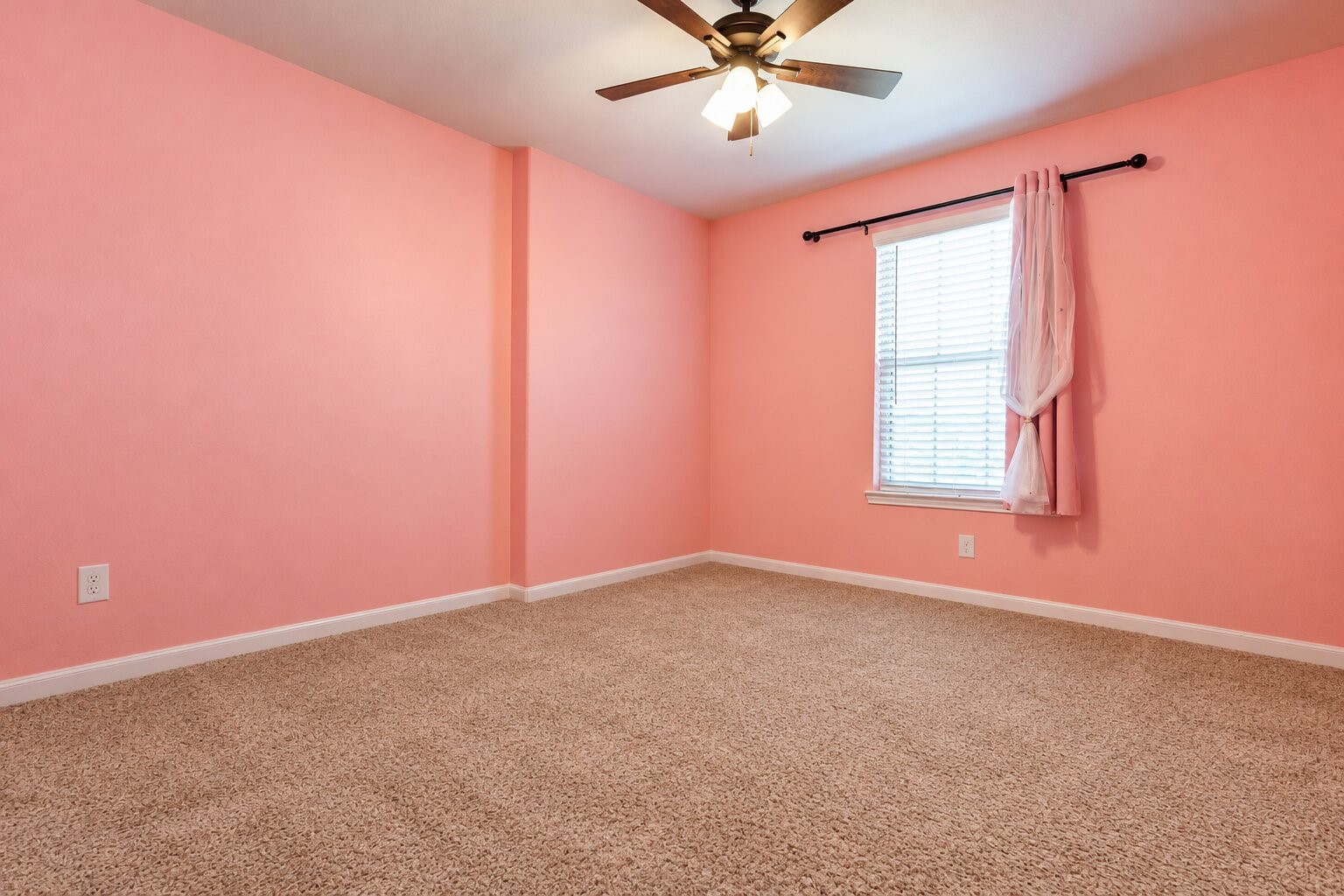 A bedroom with a ceiling fan, a big window with blinds and carpet in a warm neutral tone. A full-size bed, nightstand and dresser fit easily, with room left over for a desk or play area. The room gets plenty of natural light and feels cheerful. The wall color is easy to repaint if you want something different, and the layout makes furniture placement straightforward. There is plenty of wall space for art and photos. Photo has been digitally decluttered.