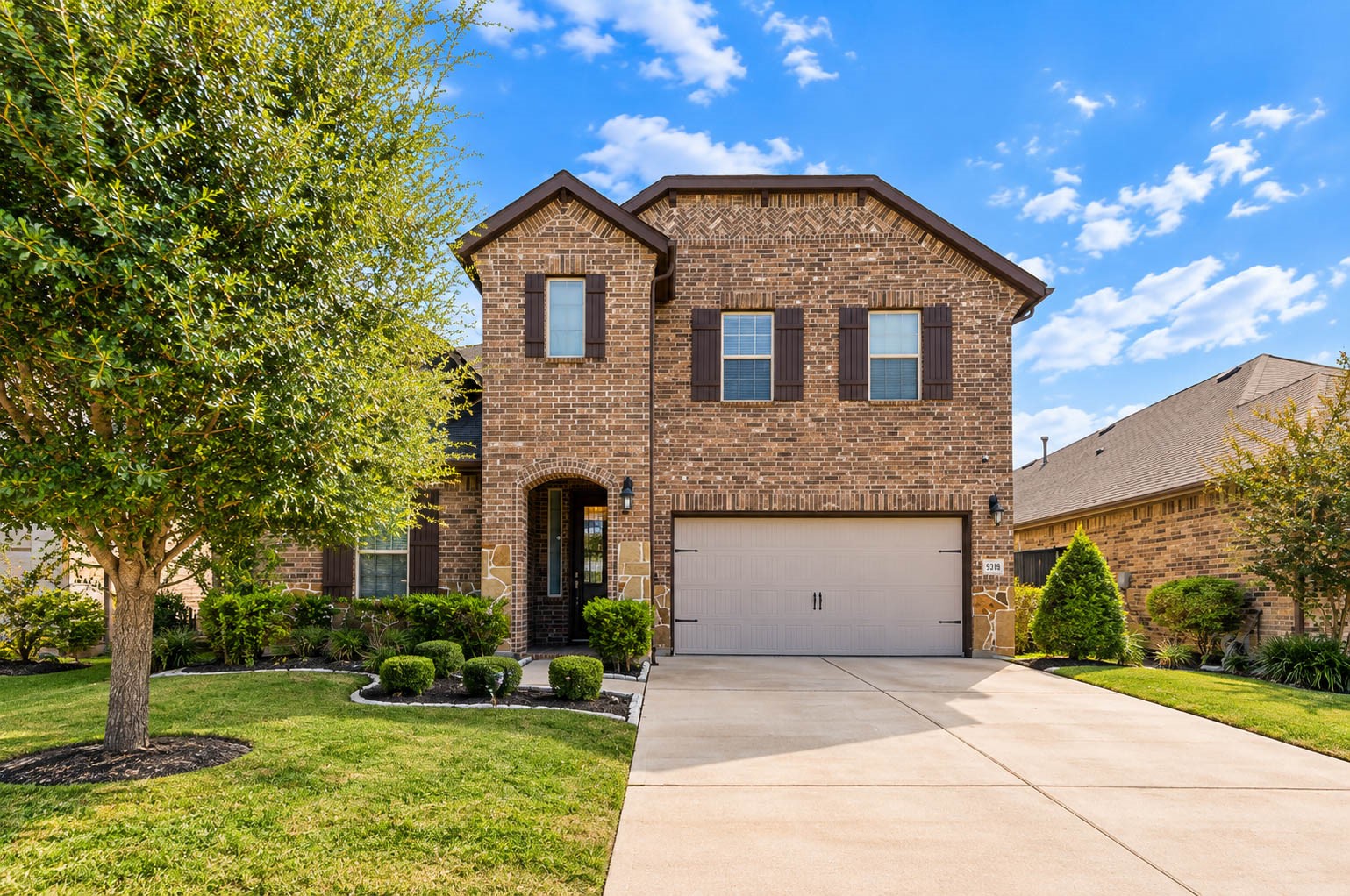 Straight-on front elevation with a covered arched entry, dark shutters on the upstairs windows and a wide driveway leading to the garage. Brick covers the full facade, which keeps maintenance low and gives the house a classic look. Landscaping beds line the walkway and a mature tree adds shade on the left. The proportions are balanced and welcoming, and the clear blue Texas sky makes the colors pop. Straight-on front elevation with a covered arched entry, dark shutters on the upstairs windows and a wide driveway leading to the garage. Brick covers the full facade, which keeps maintenance low and gives the house a classic look. Landscaping beds line the walkway and a mature tree adds shade on the left. The proportions are balanced and welcoming, and the clear blue Texas sky makes the colors pop.