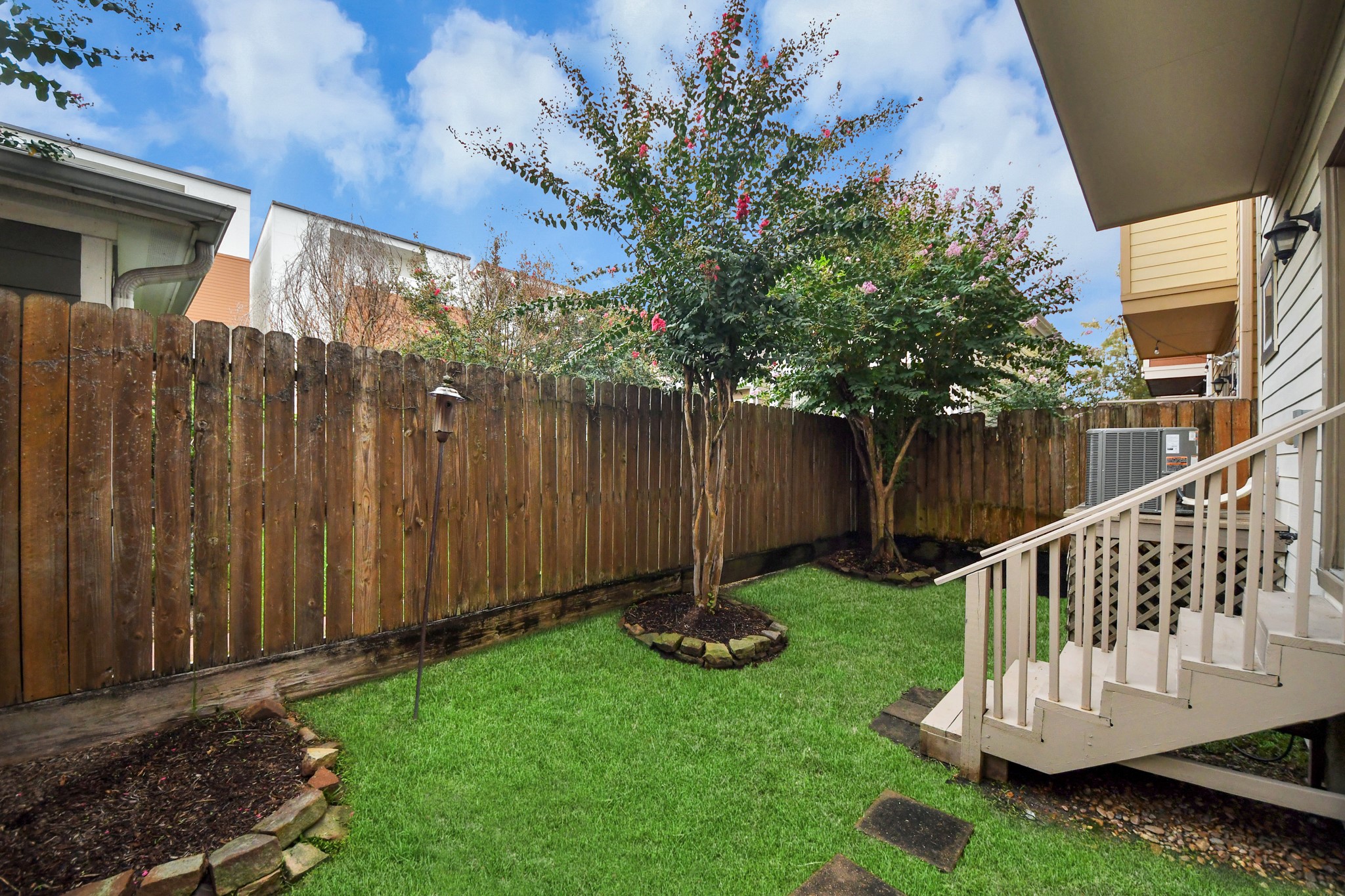 Charming backyard with grass, mature trees, and a cozy wooden fence providing privacy and a space to relax and enjoy the outdoors, in the heart of the city!