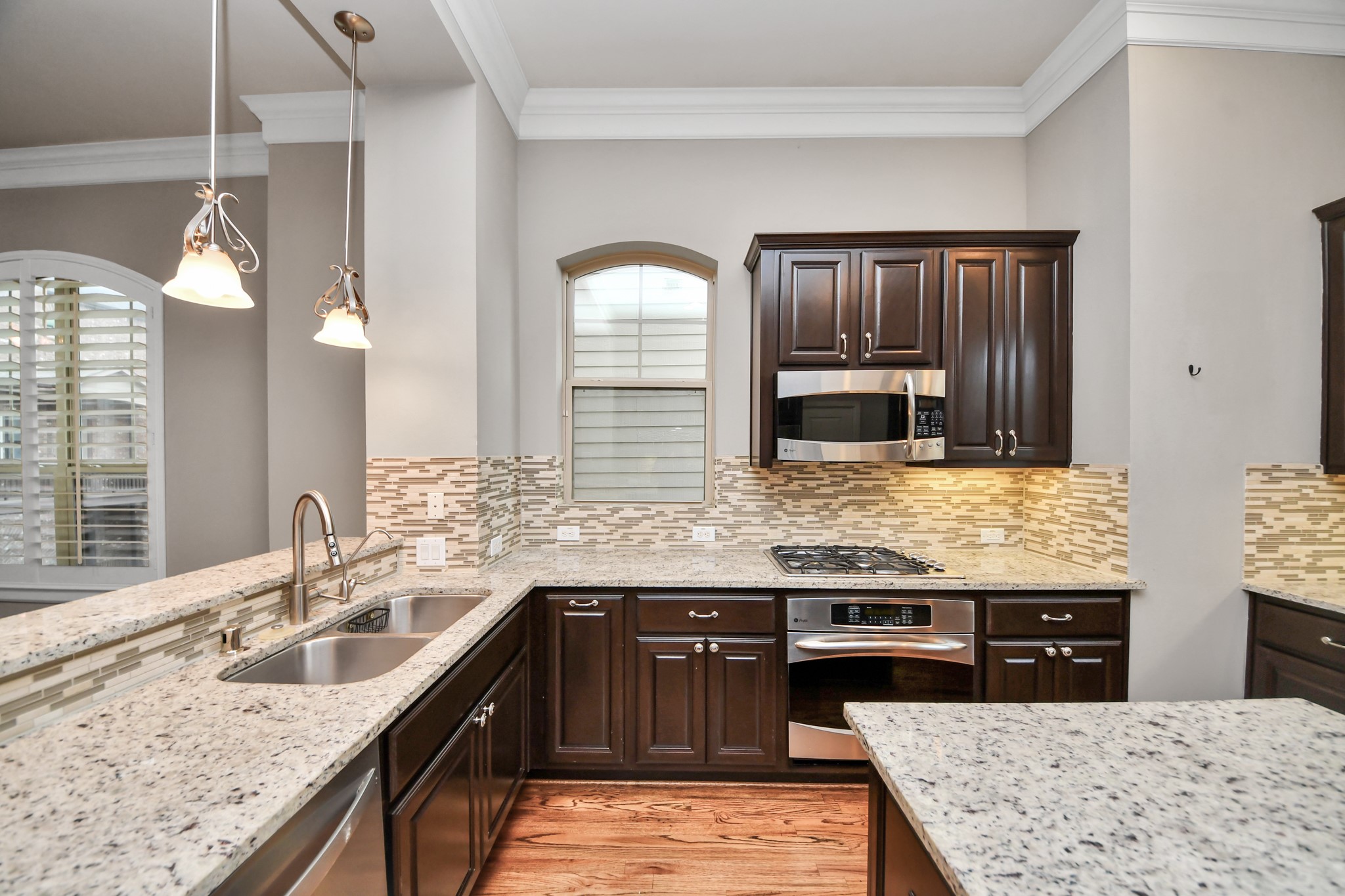 Elegant kitchen featuring dark wood cabinetry, granite countertops, and modern stainless steel appliances, complemented by a stylish tile backsplash.