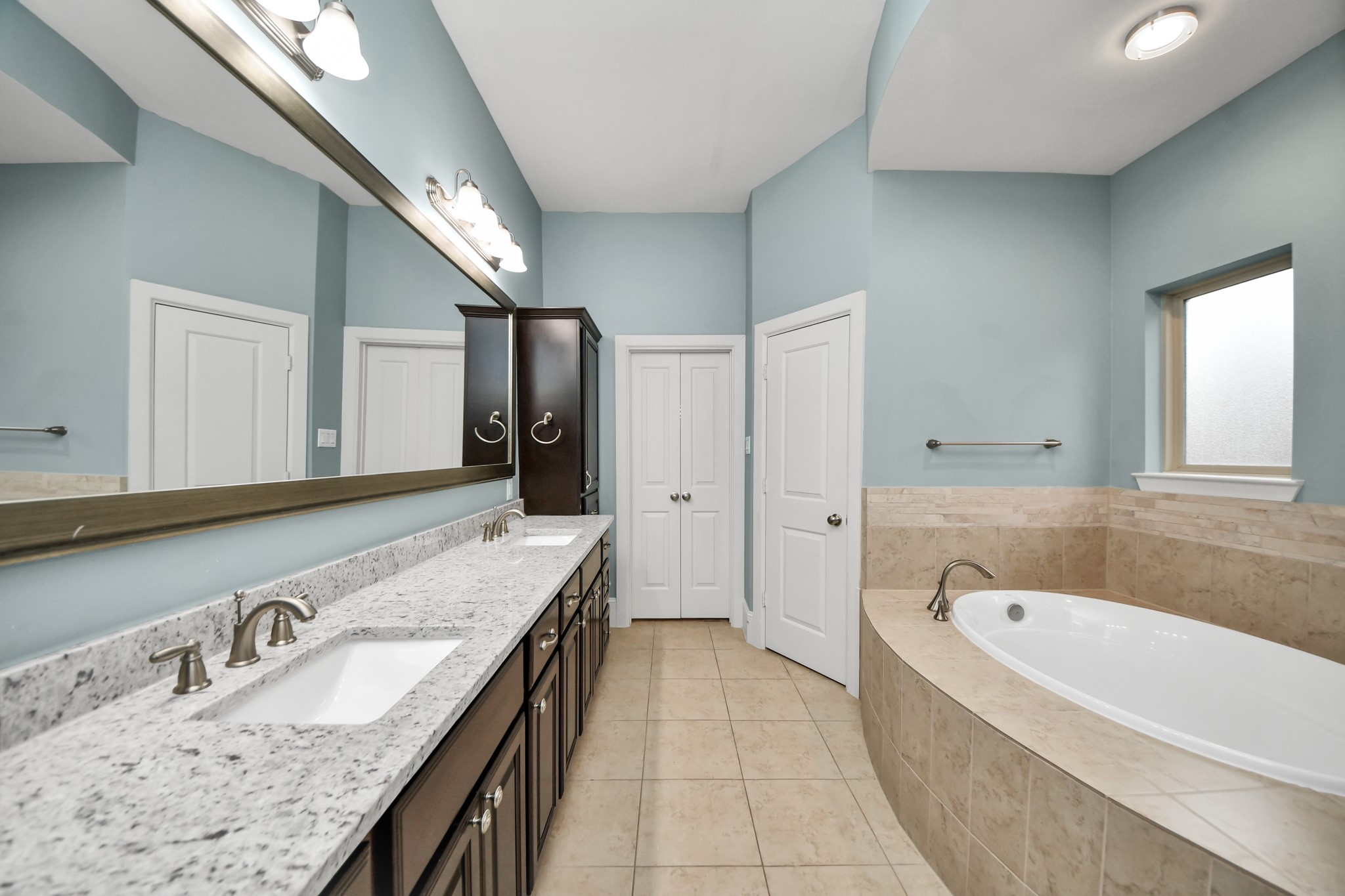 Experience luxury in the primary bathroom, featuring a spacious dual-sink vanity, elegant granite countertops, and a relaxing soaking tub surrounded by serene blue walls.
