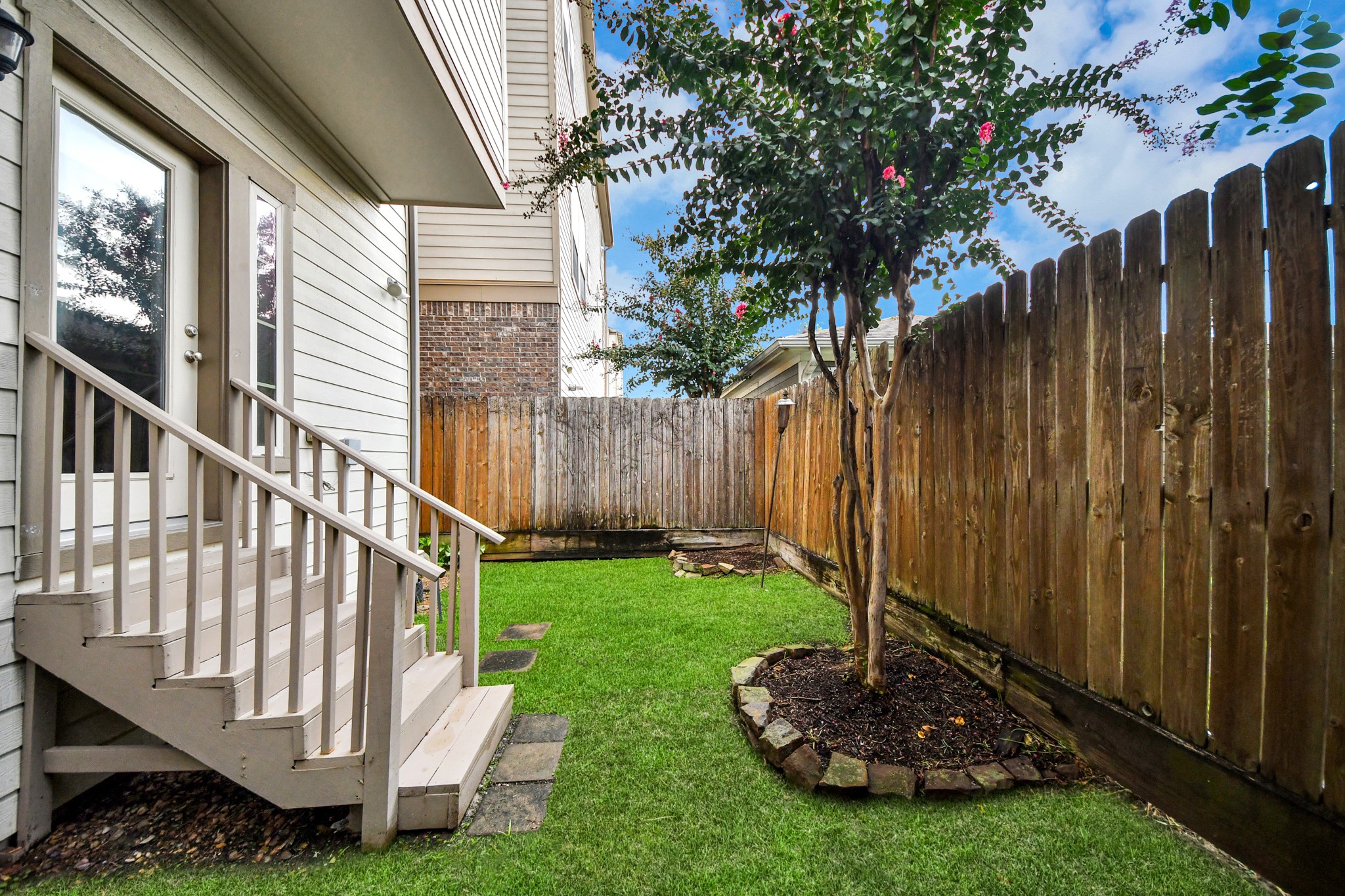 Charming backyard space with lush green grass, a blooming tree, and a privacy fence, perfect for relaxing or entertaining.