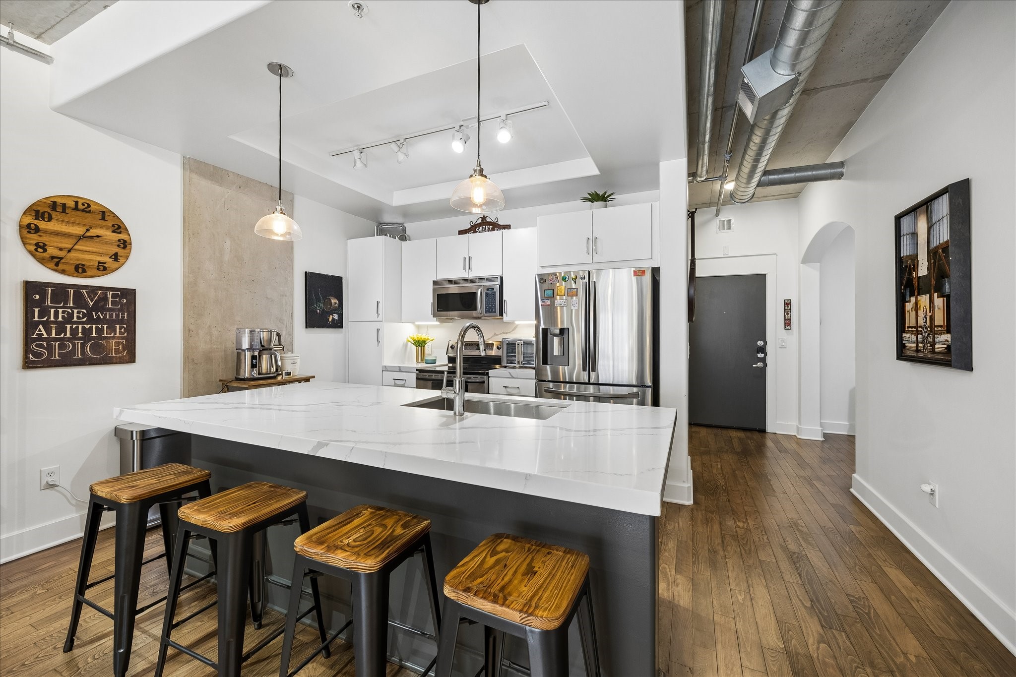 The kitchen featuring a large quartz island with seating, stainless steel appliances, and stylish exposed duct work to add that industrial vibe.
