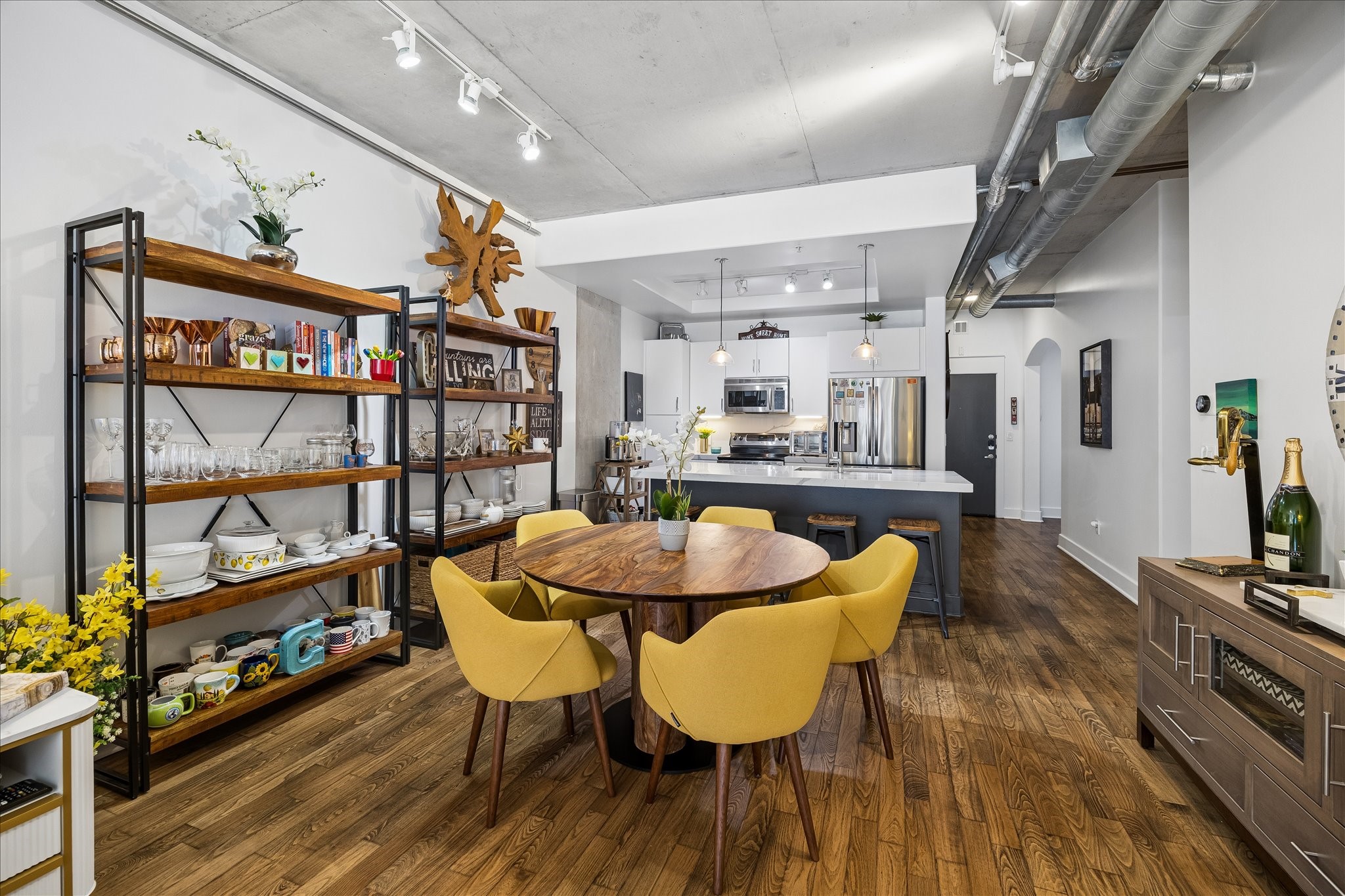 Stylish open-plan dining and kitchen area featuring sleek hardwood floors, vibrant yellow chairs, and industrial accents, perfect for modern living and entertaining. Stylish open-plan dining and kitchen area featuring sleek hardwood floors, vibrant yellow chairs, and industrial accents, perfect for modern living and entertaining.