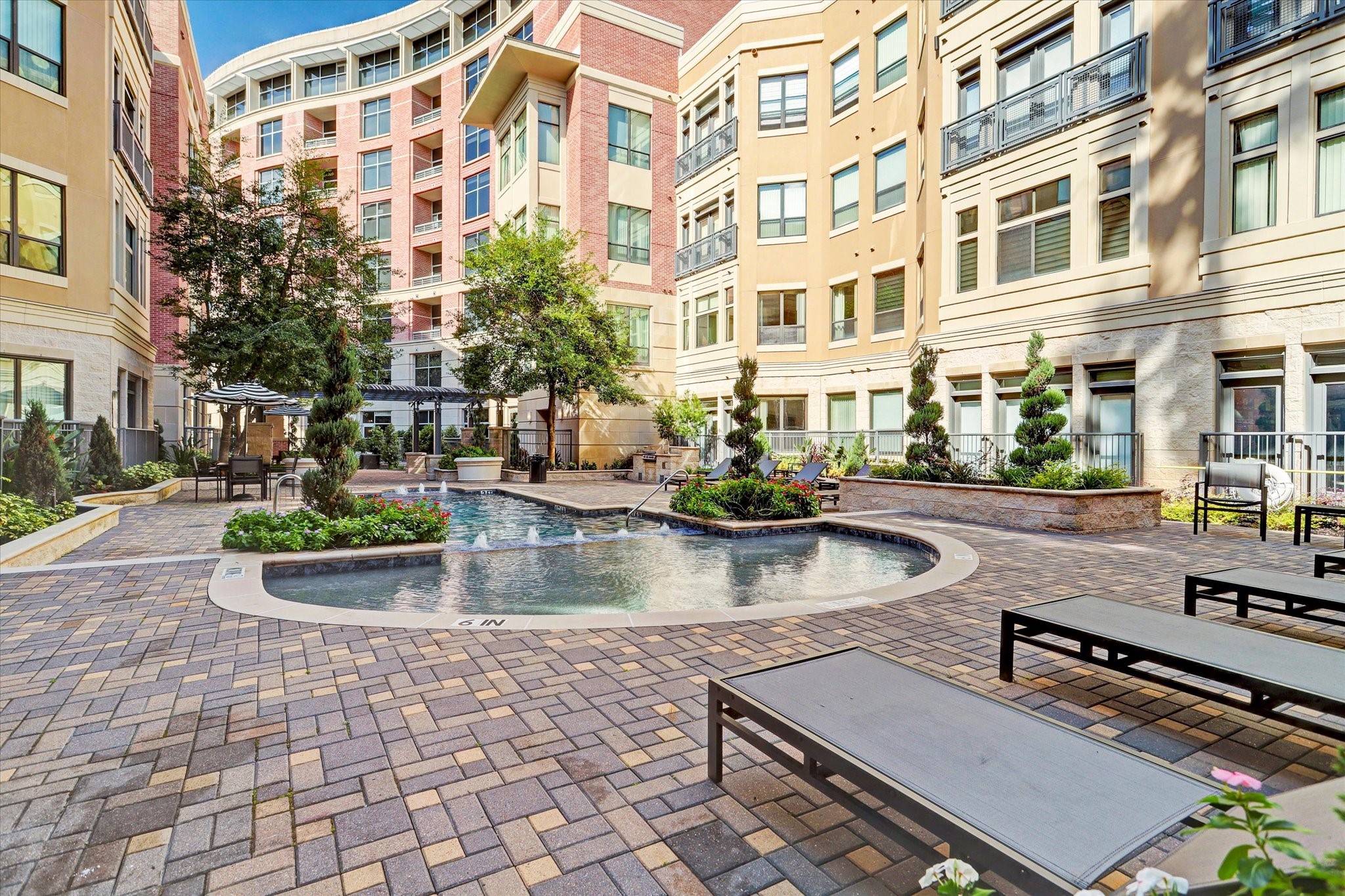 Experience luxury living with this beautifully landscaped courtyard featuring a serene pool, surrounded by elegant architecture and ample seating for relaxation.