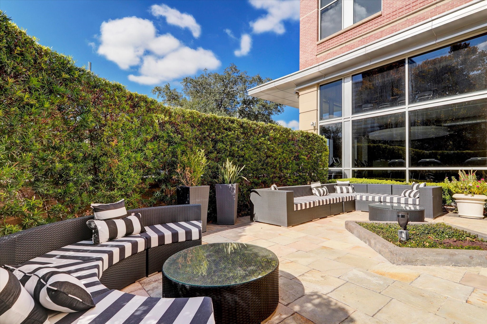 Elegant outdoor patio featuring chic striped seating, lush greenery, and ample space for relaxation or entertaining against a backdrop of large windows.