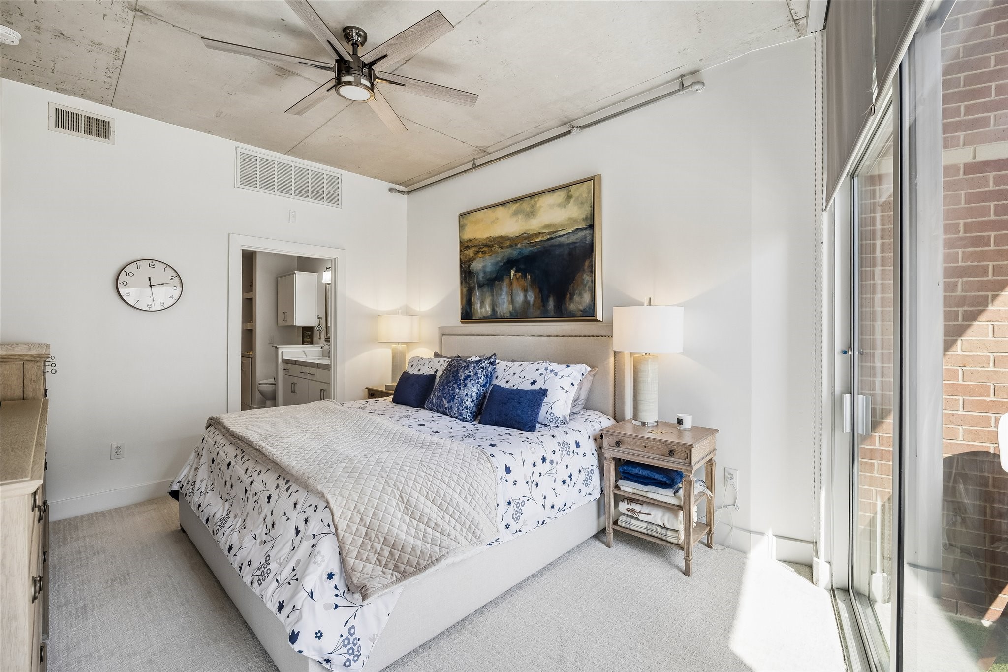 Bright and inviting bedroom featuring large glass doors leading to a balcony, complemented by a cozy bed with patterned bedding and a modern ceiling fan.