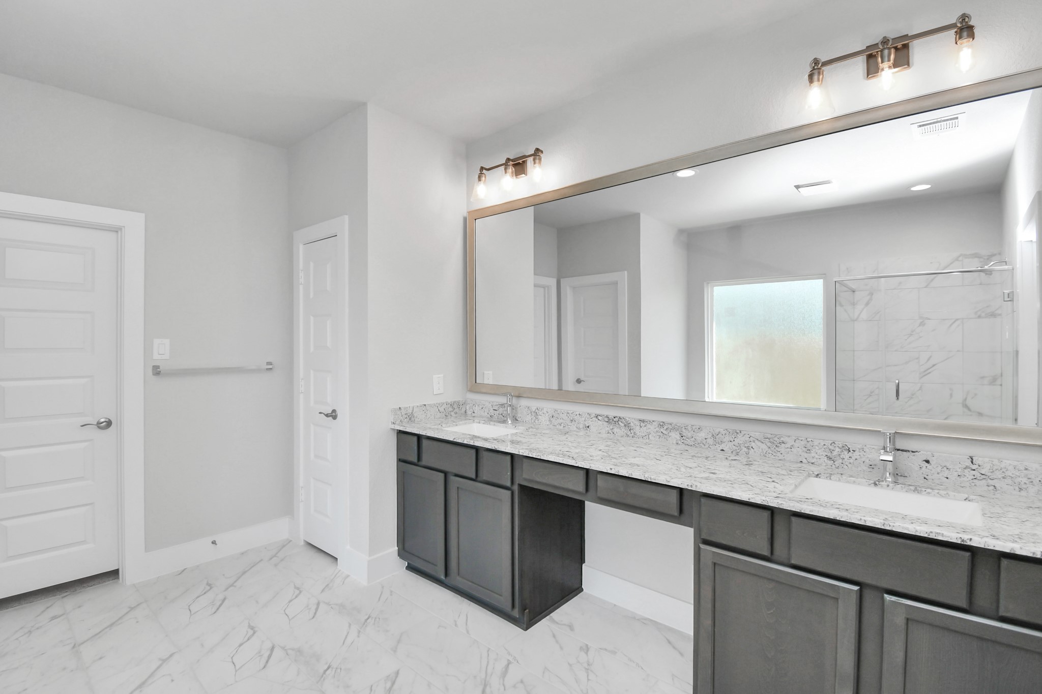 Escape to a spa-like oasis in this primary bathroom. Enjoy a walk-in shower with tile surround, a separate garden tub with custom detailing, and an elegant vanity featuring light countertops, modern hardware, and beautiful vanity lights. Experience luxury and relaxation in every detail. Sample photo of completed home with similar floor plan. Actual colors and selections may vary.