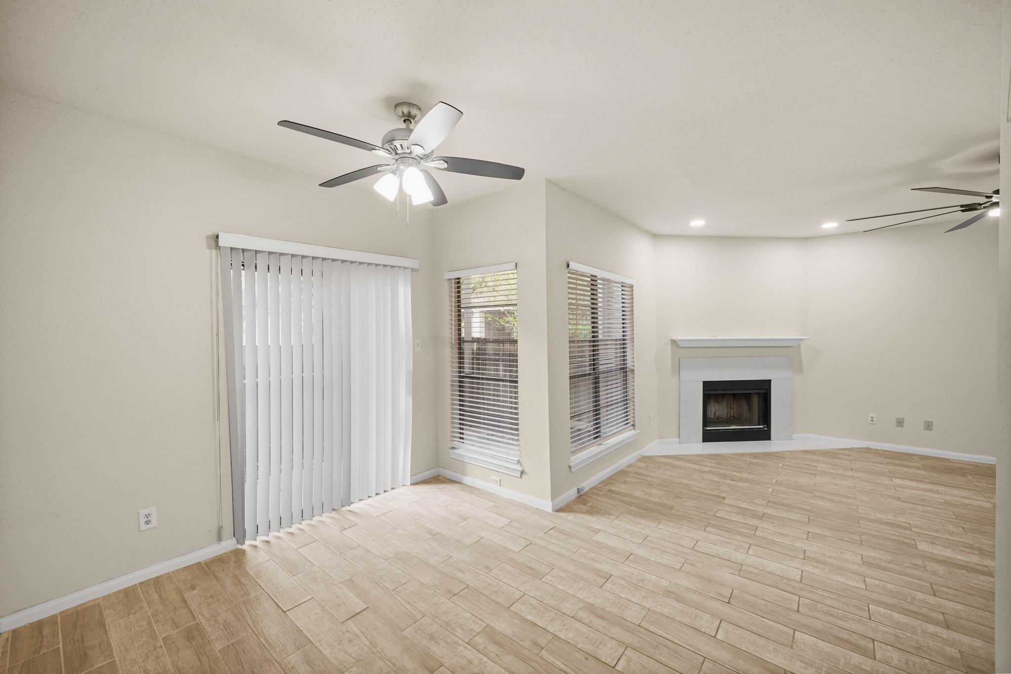 View of the living area and dining area. Fireplace in living area, and ceiling fans for comfort. Natural light pours in through large windows and sliding glass doors that lead to a fenced patio area.