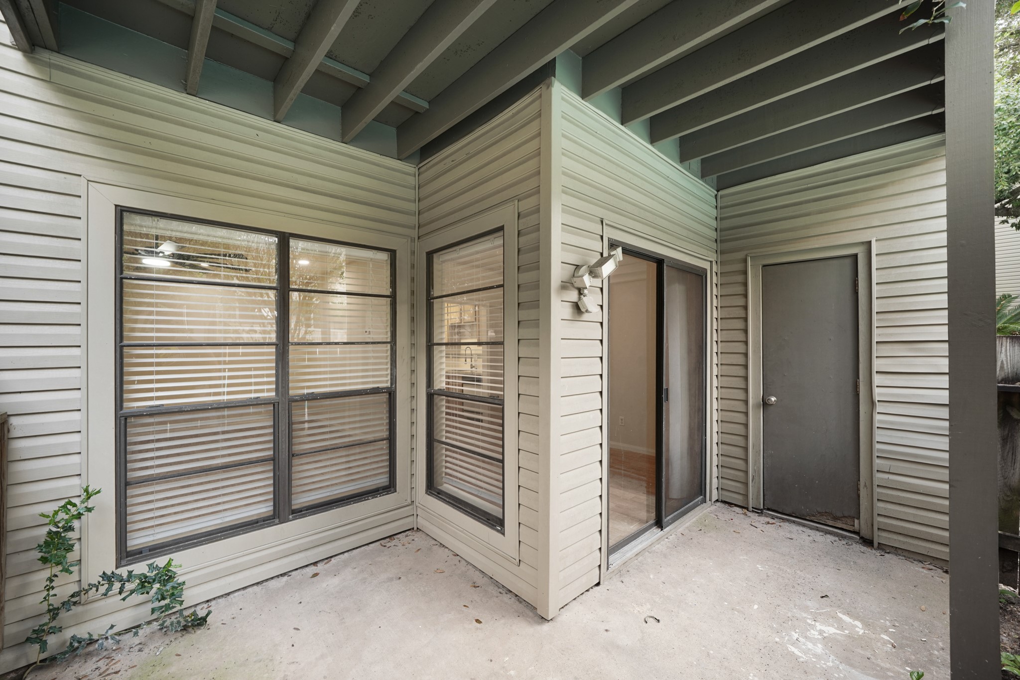 Small, covered patio area featuring sliding glass doors and large windows that allow natural light to enter. It offers a private outdoor space with unless potential.