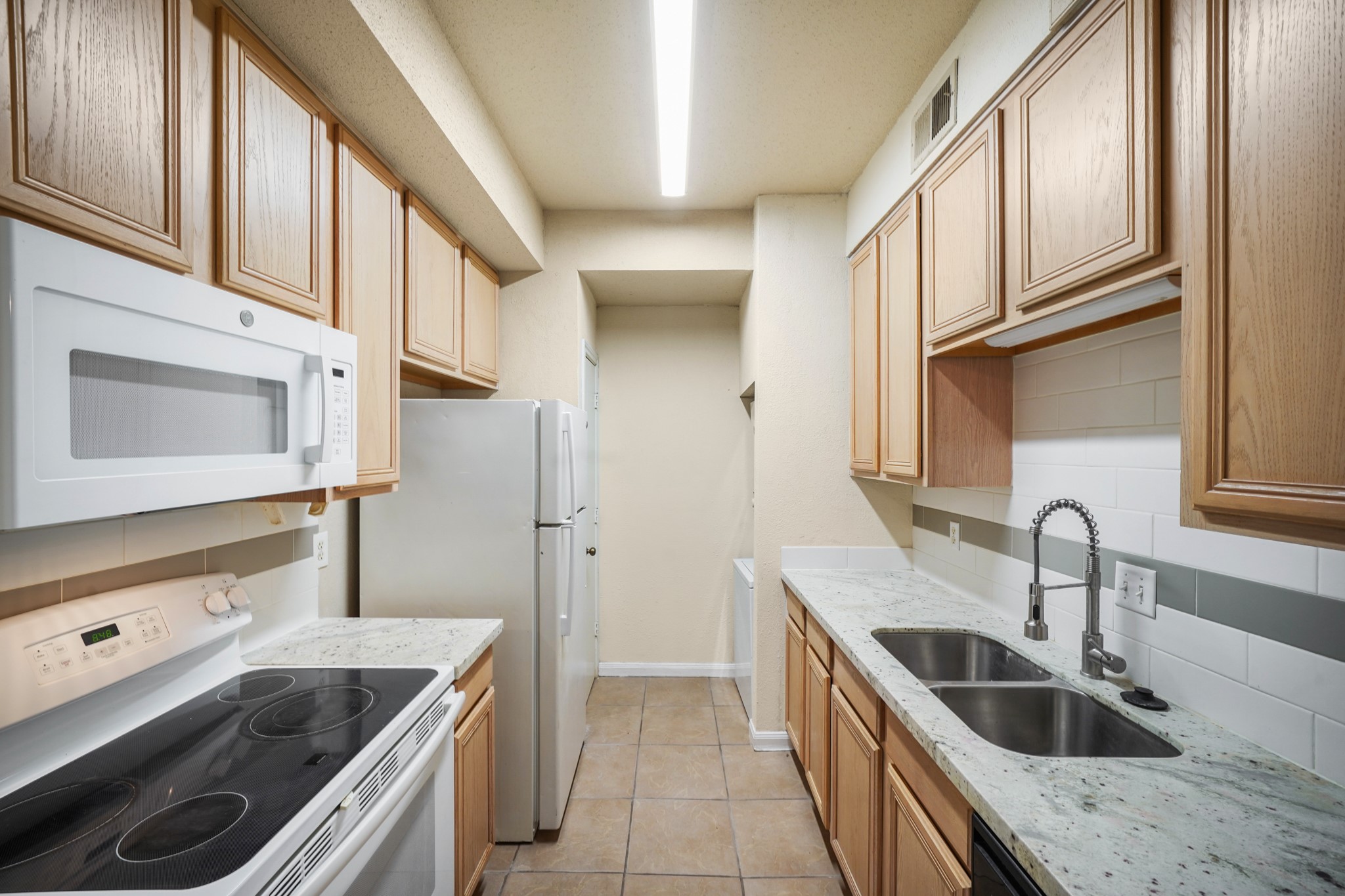 This kitchen features a microwave, refrigerator and stove. It has a double sink with a sleek faucet and tiled flooring, offering a functional and clean design.