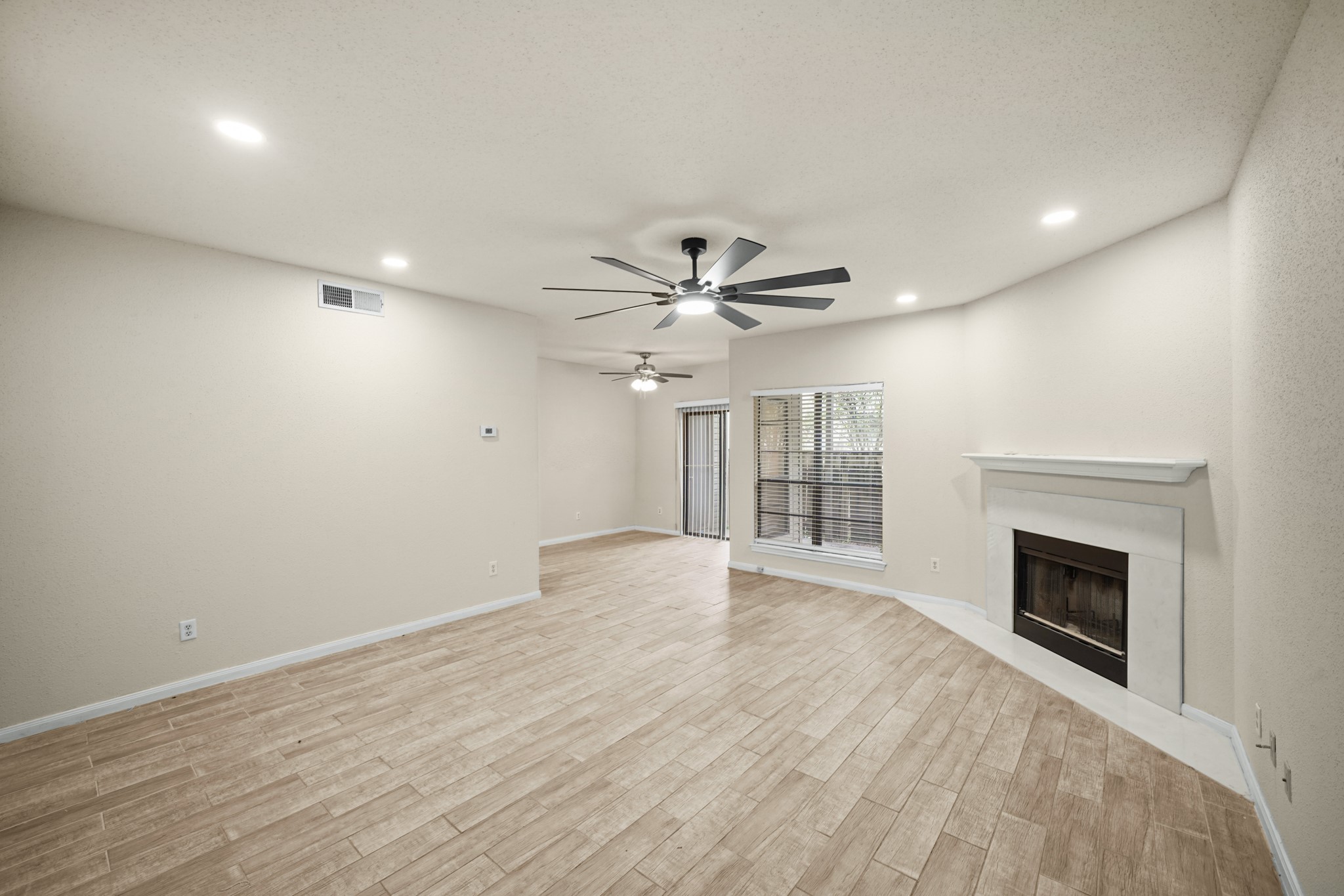 Living area features a modern ceiling fan, recessed lighting, and a cozy fireplace.  Large windows allow for natural light, with sliding doors leading to a fenced patio area.