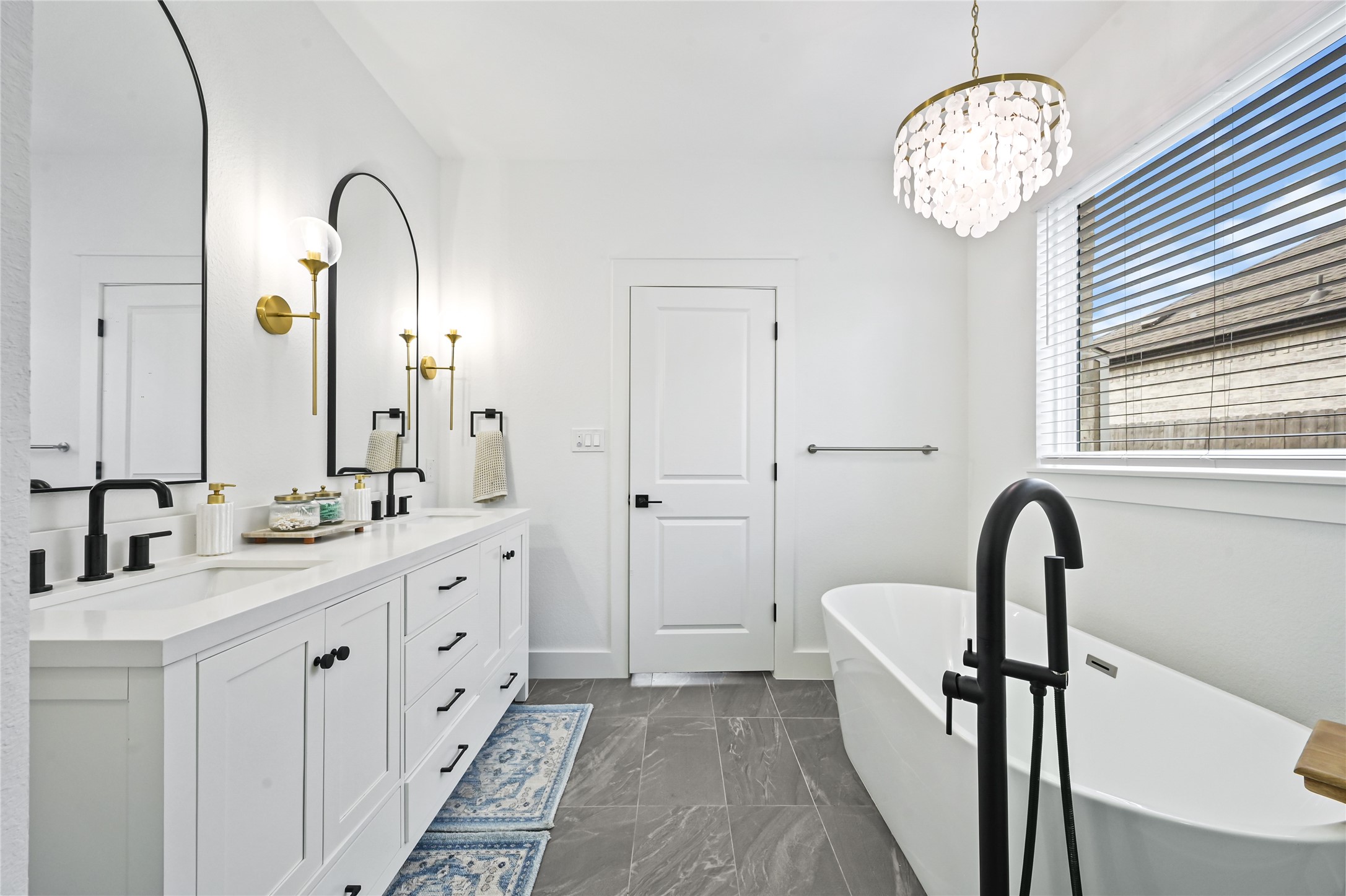The spacious layout features a gorgeous double-sink vanity with crisp white cabinetry, sleek black fixtures, and elegant arched mirrors