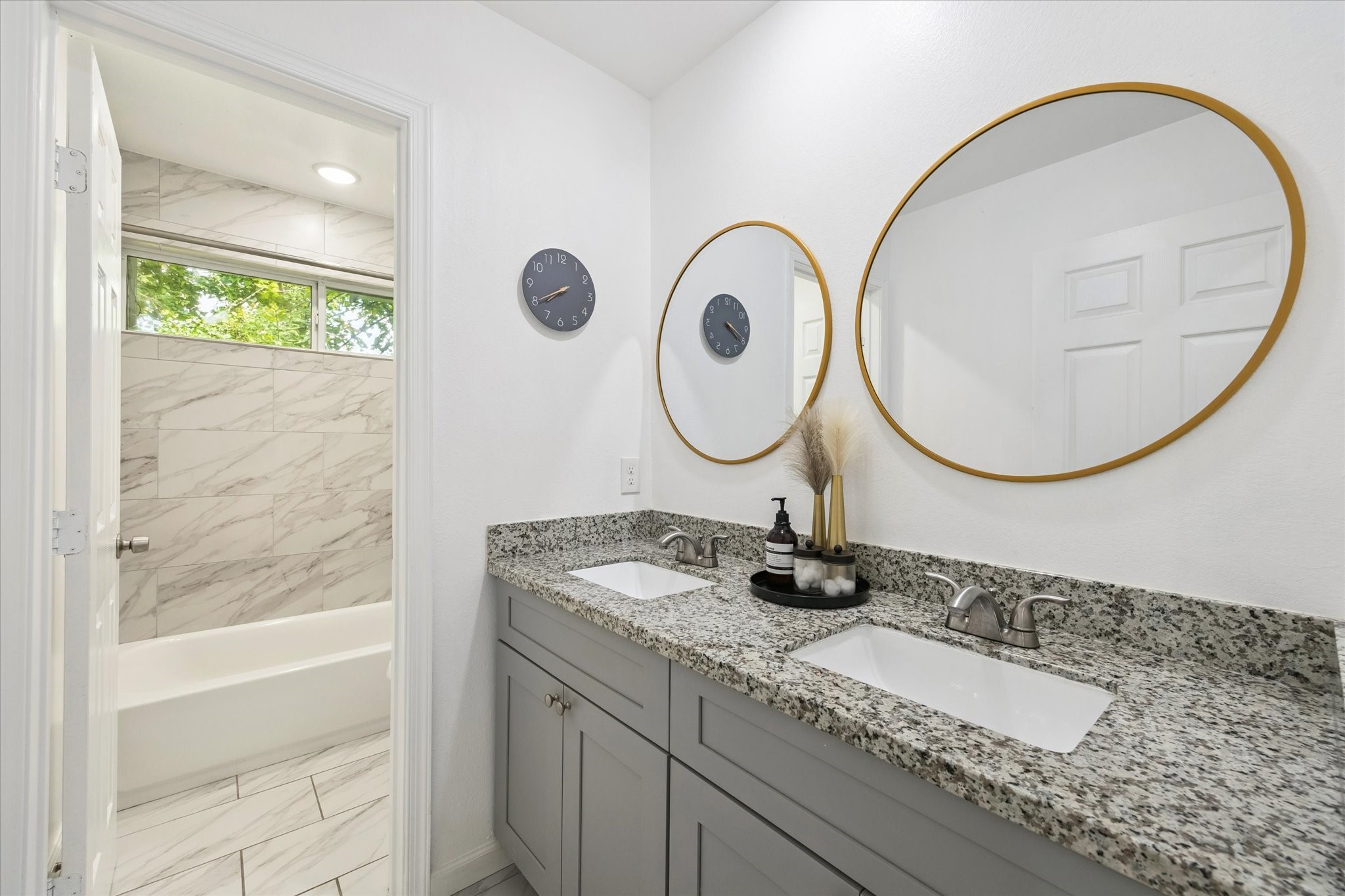 The secondary bathroom is designed for convenience with dual sinks, granite counters, and framed mirrors. A separate space for the tub and shower provides privacy and functionality for shared use.