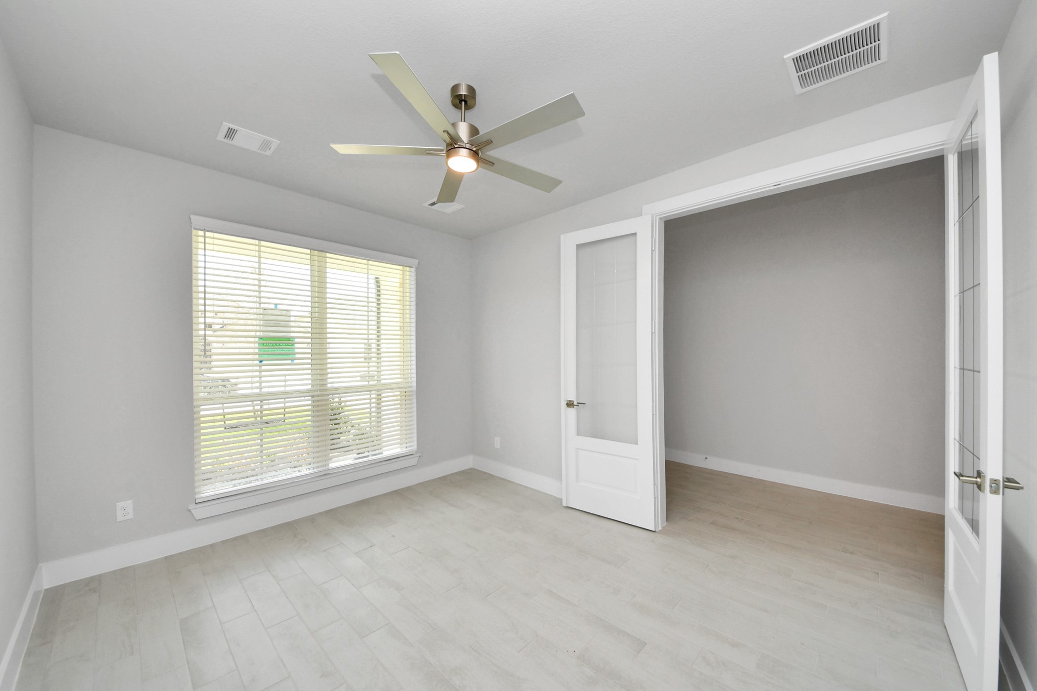Experience the perfect blend of sophistication and warmth in this home office, boasting elegant wood-look tile flooring and flooded with natural light from expansive windows and French doors. Sample photo of completed home with similar floor plan. Actual colors and selections may vary.