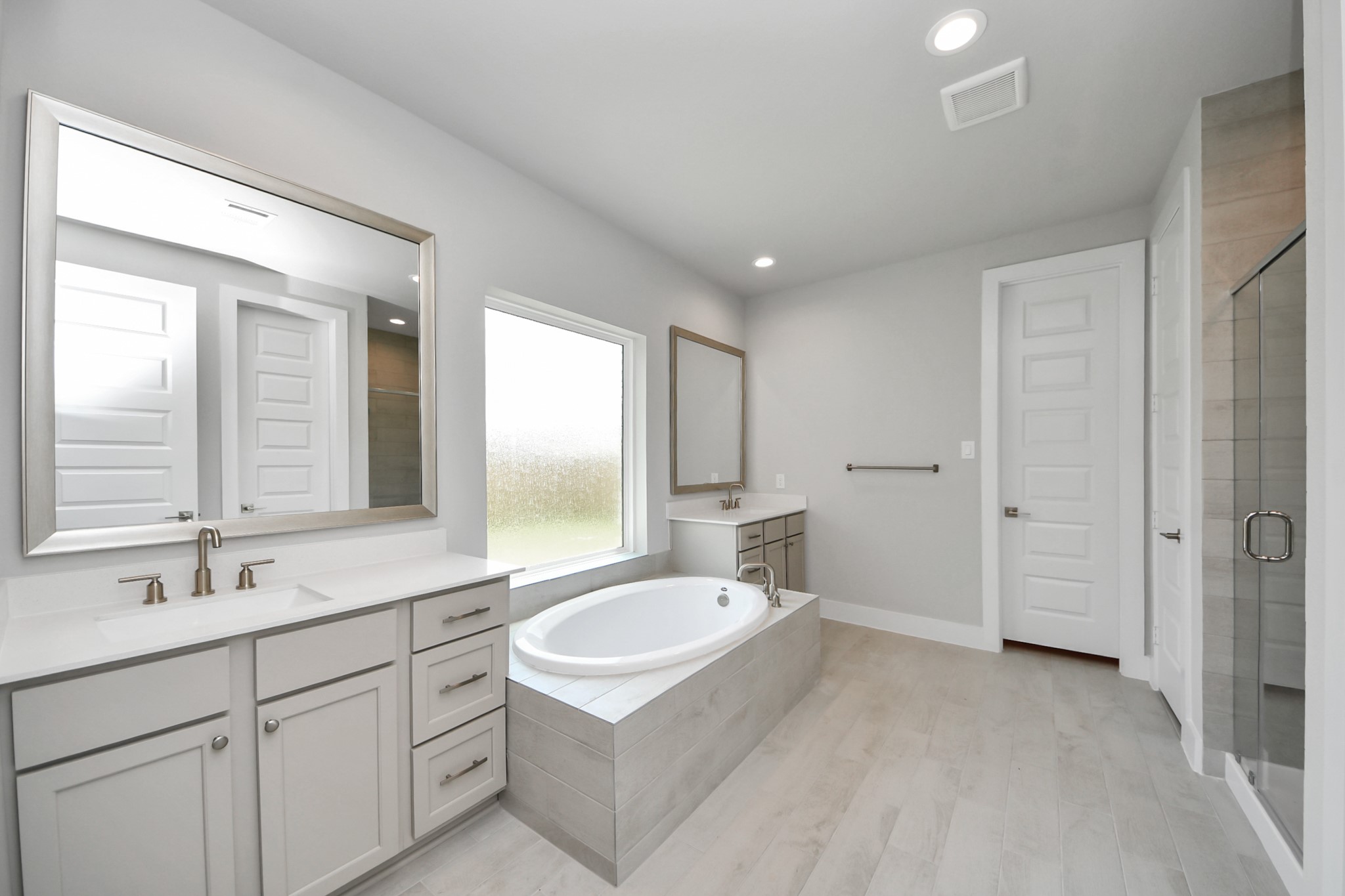 Escape to a spa-like oasis in this primary bathroom. Enjoy a walk-in shower with tile surround, a separate garden tub with custom detailing, and an elegant vanity featuring light countertops, modern hardware, and beautiful recessed lights. Experience luxury and relaxation in every detail. Sample photo of completed home with similar floor plan. Actual colors and selections may vary.