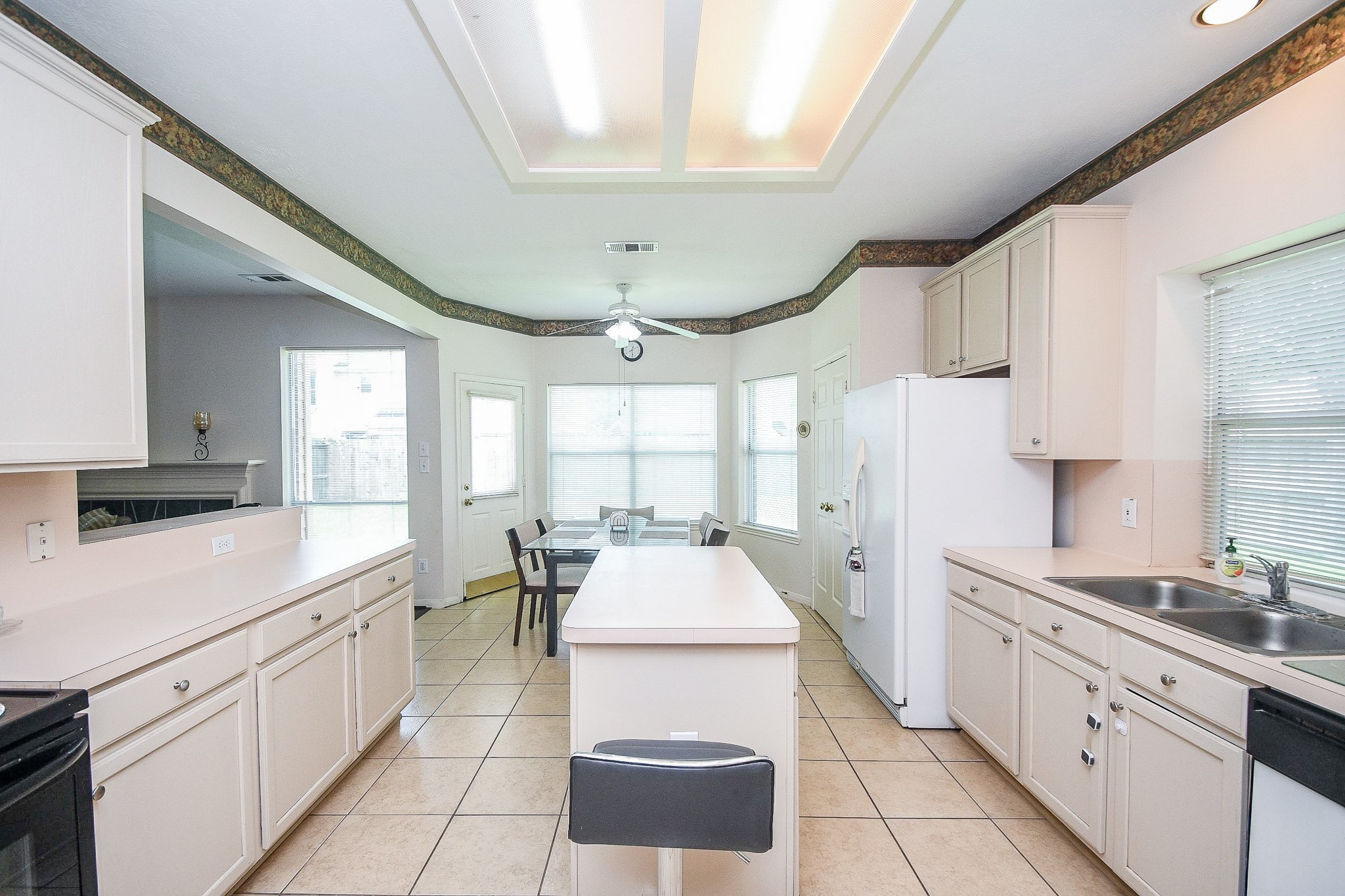 Bright and spacious kitchen with ample cabinetry, a central island, and tile flooring. It features a breakfast area with large windows for natural light, and a ceiling fan for comfort.