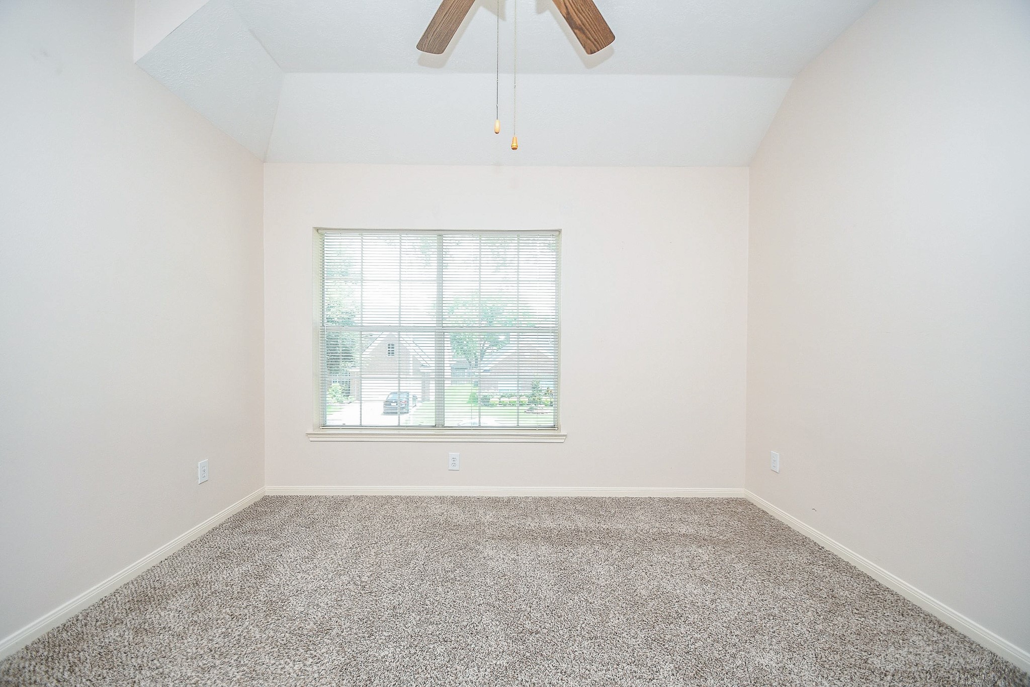 This room features neutral walls, plush carpet, and a large window for natural light. A ceiling fan provides comfort and the space is versatile for various uses.