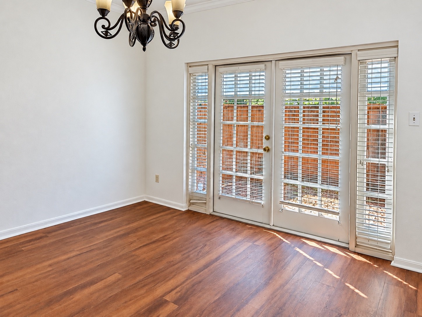 Natural lit dining area with wood-look flooring, a decorative chandelier,French doors opening to the peaceful private fenced patio.
