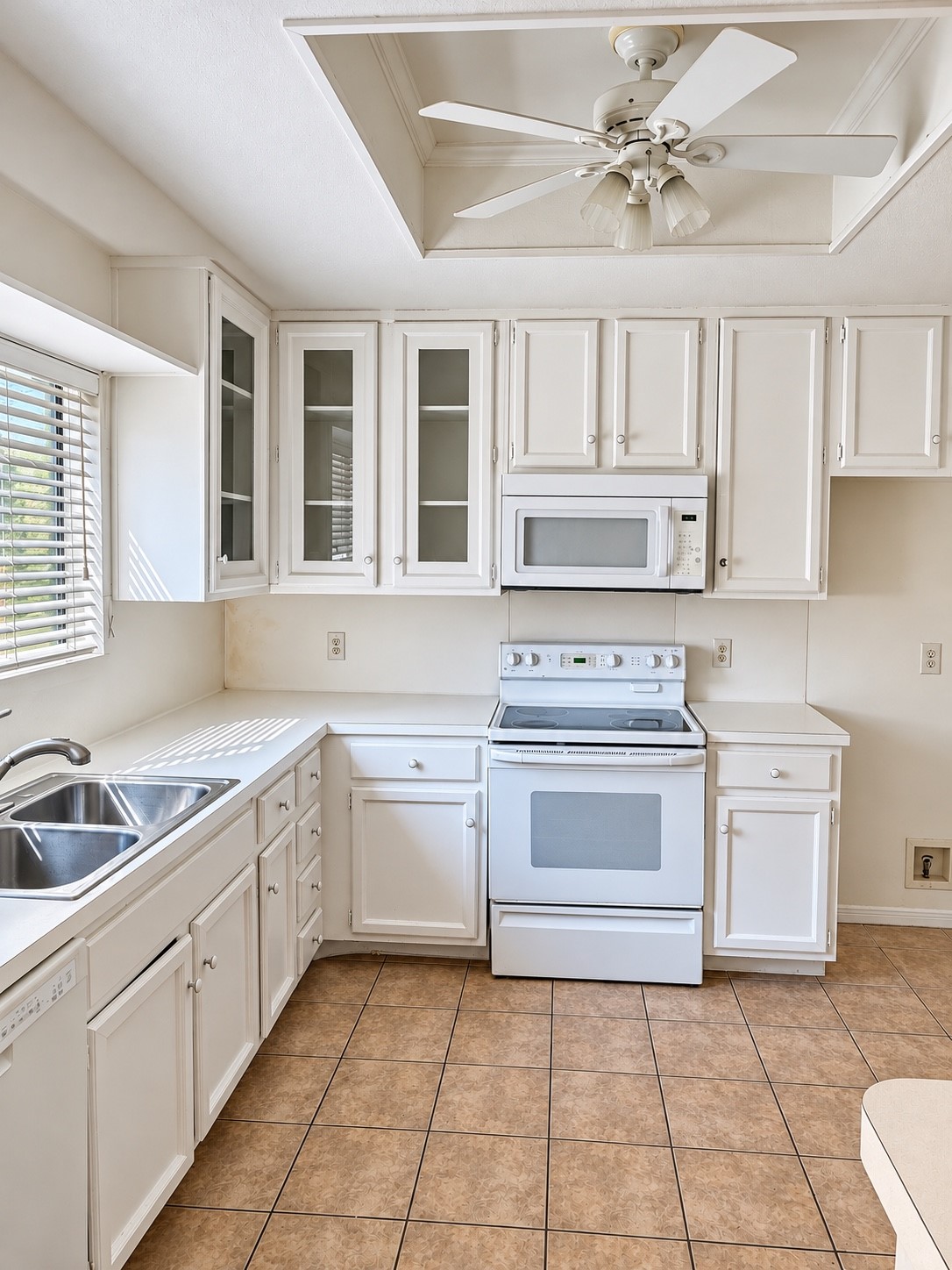 Light filled kitchen with white cabinetry, glass front accents, ample counter space and tile flooring.
