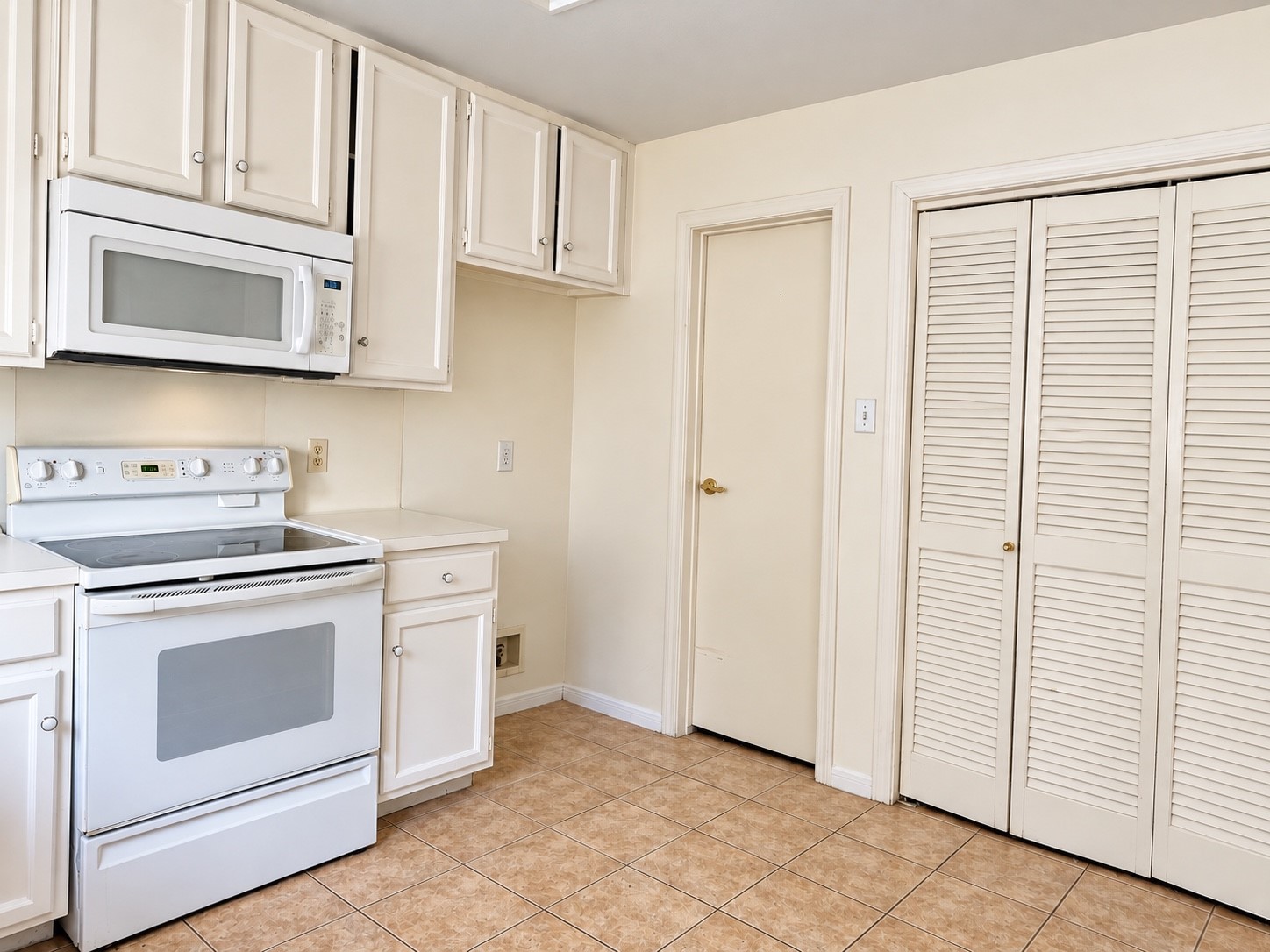 Charming kitchen with white cabinetry, an electric range, built-in-microwave, easy care tile fooring, with access to spacious pantry, easy access utility room