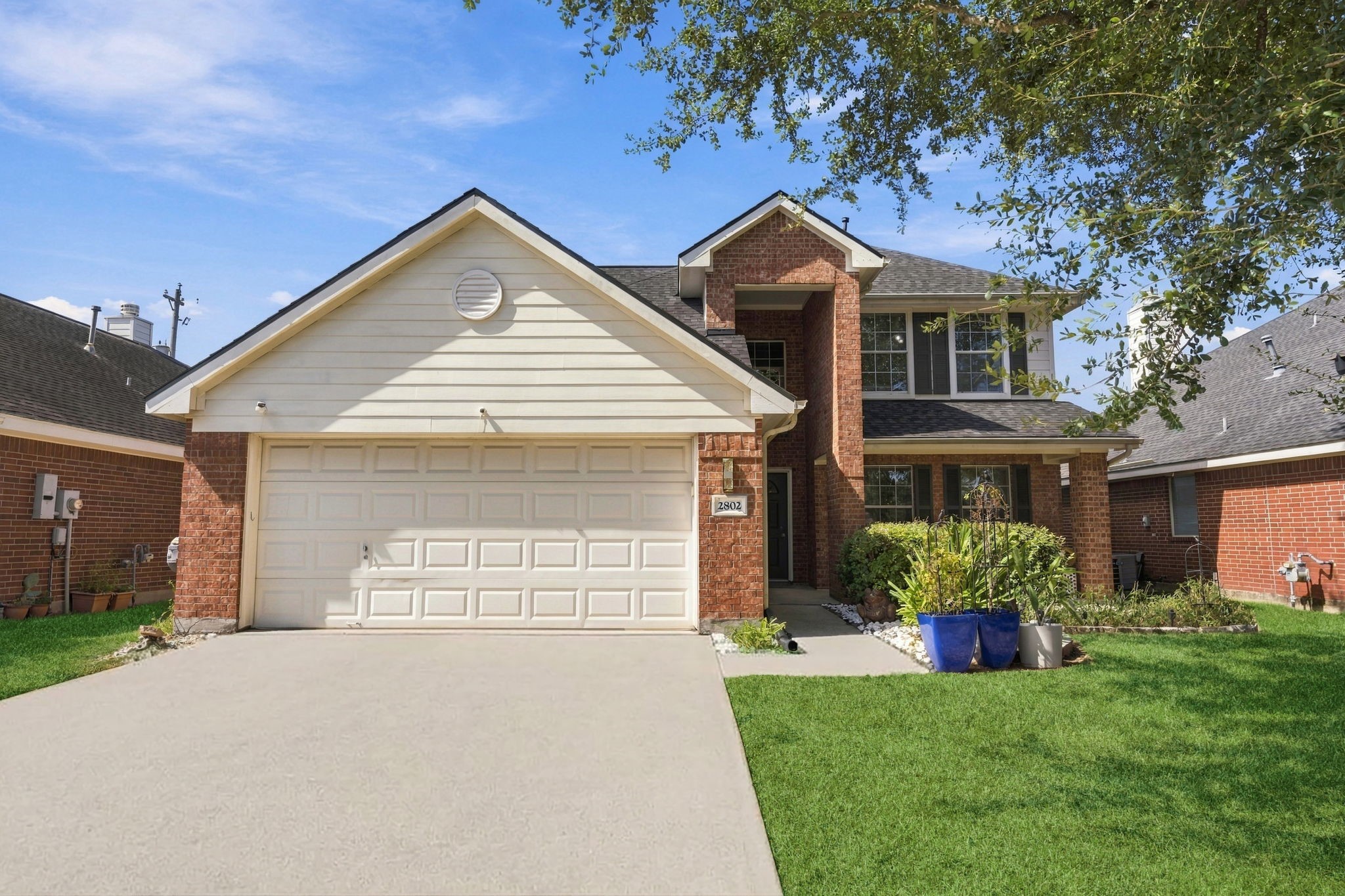 Charming two-story brick home with a spacious two-car garage, manicured lawn, and inviting front porch.