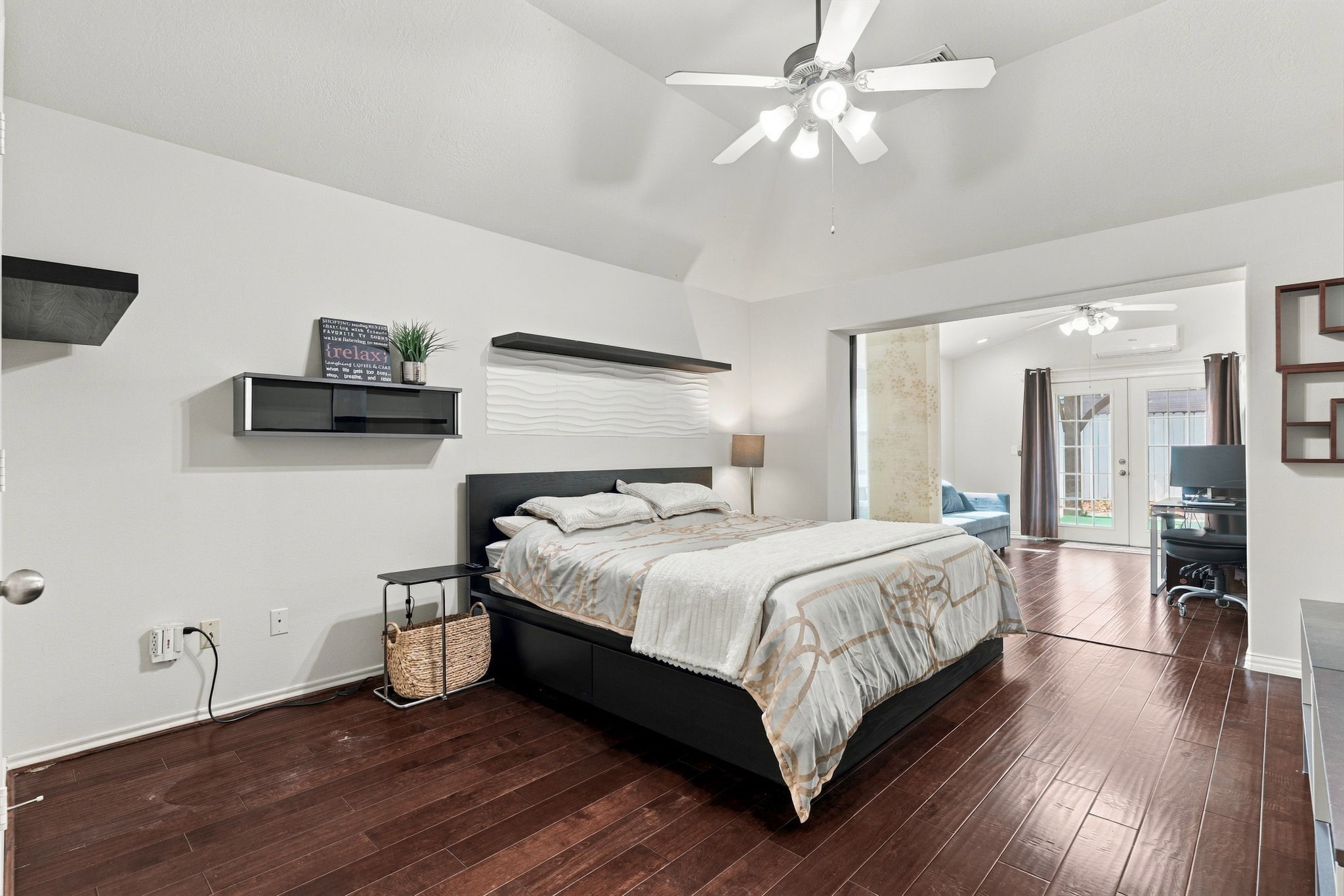 Spacious bedroom featuring elegant hardwood floors, modern ceiling fan, and a cozy sitting area with French doors leading to a bright office space.
