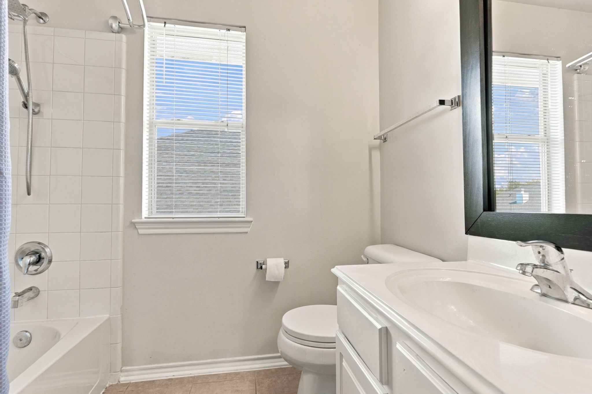 Bright and inviting bathroom featuring a clean white vanity, a bathtub with tile surround, and ample natural light from two windows.