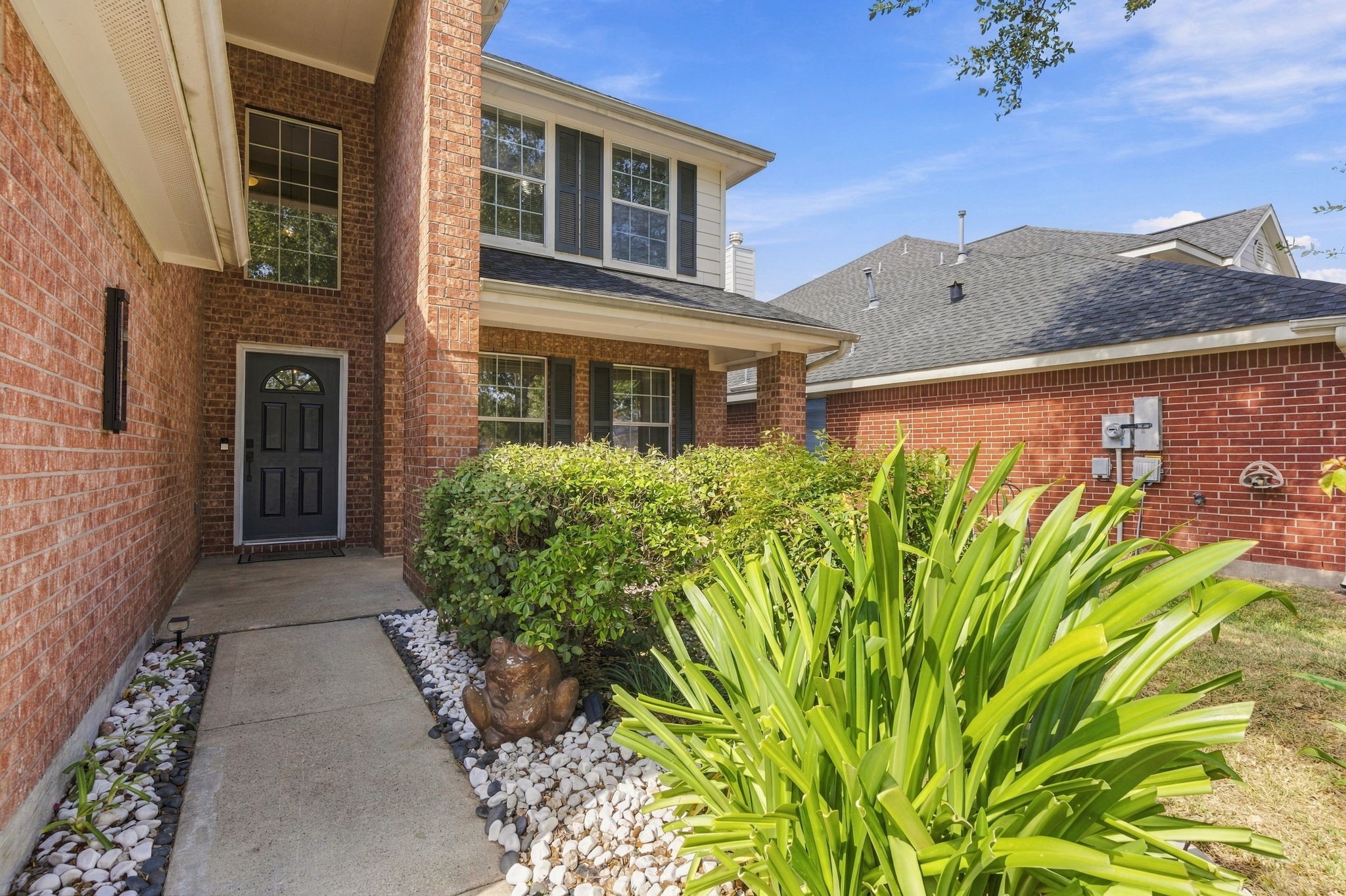 Charming brick exterior with a welcoming walkway, lush greenery, and a stylish front door, offering great curb appeal.
