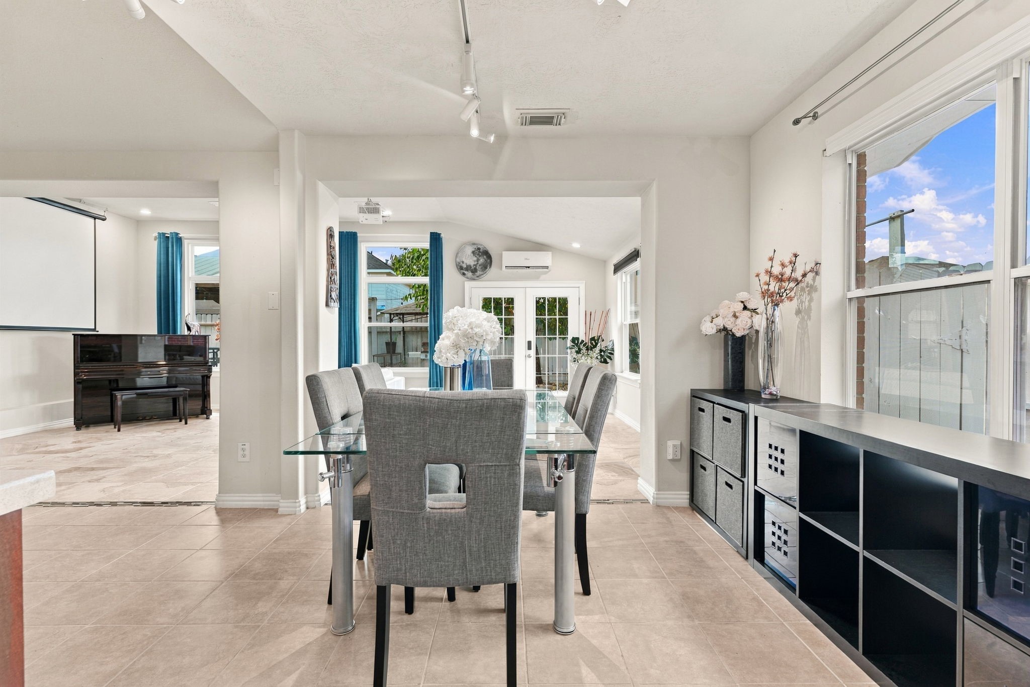 Bright and inviting dining area with a glass table and modern chairs, opening to a sunlit living space with large windows and elegant decor.