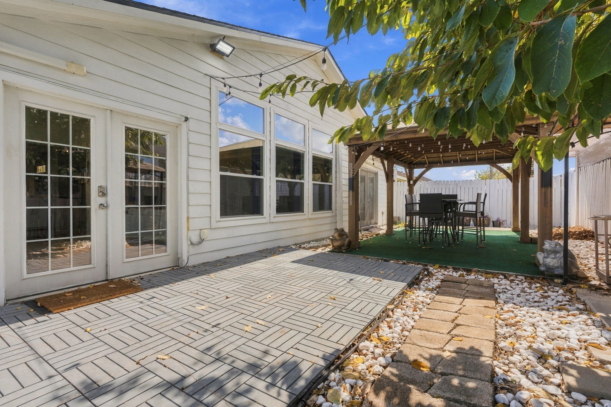 Charming backyard retreat featuring a spacious patio with elegant French doors and a cozy pergola-covered seating area, perfect for outdoor entertaining.